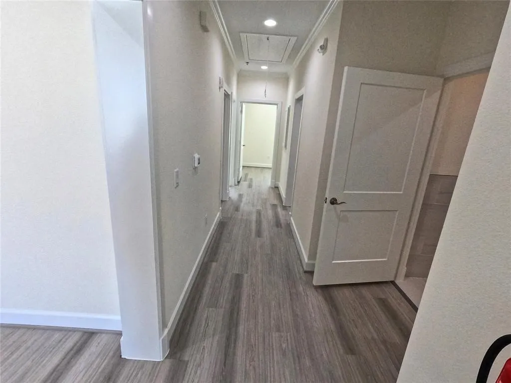 Corridor featuring attic access, wood finished floors, baseboards, and crown molding