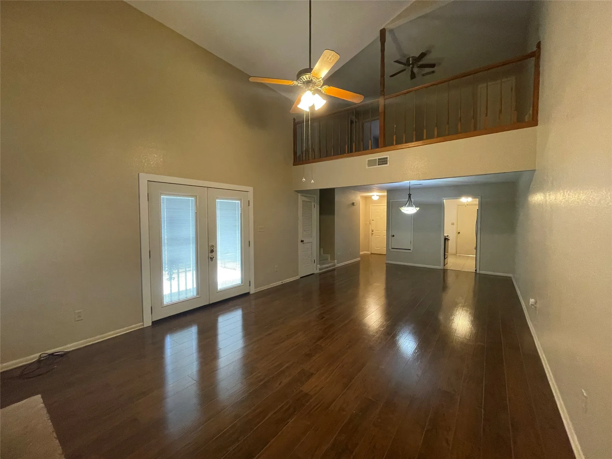 Unfurnished living room featuring baseboards, a high ceiling, ceiling fan, french doors, and wood finished floors