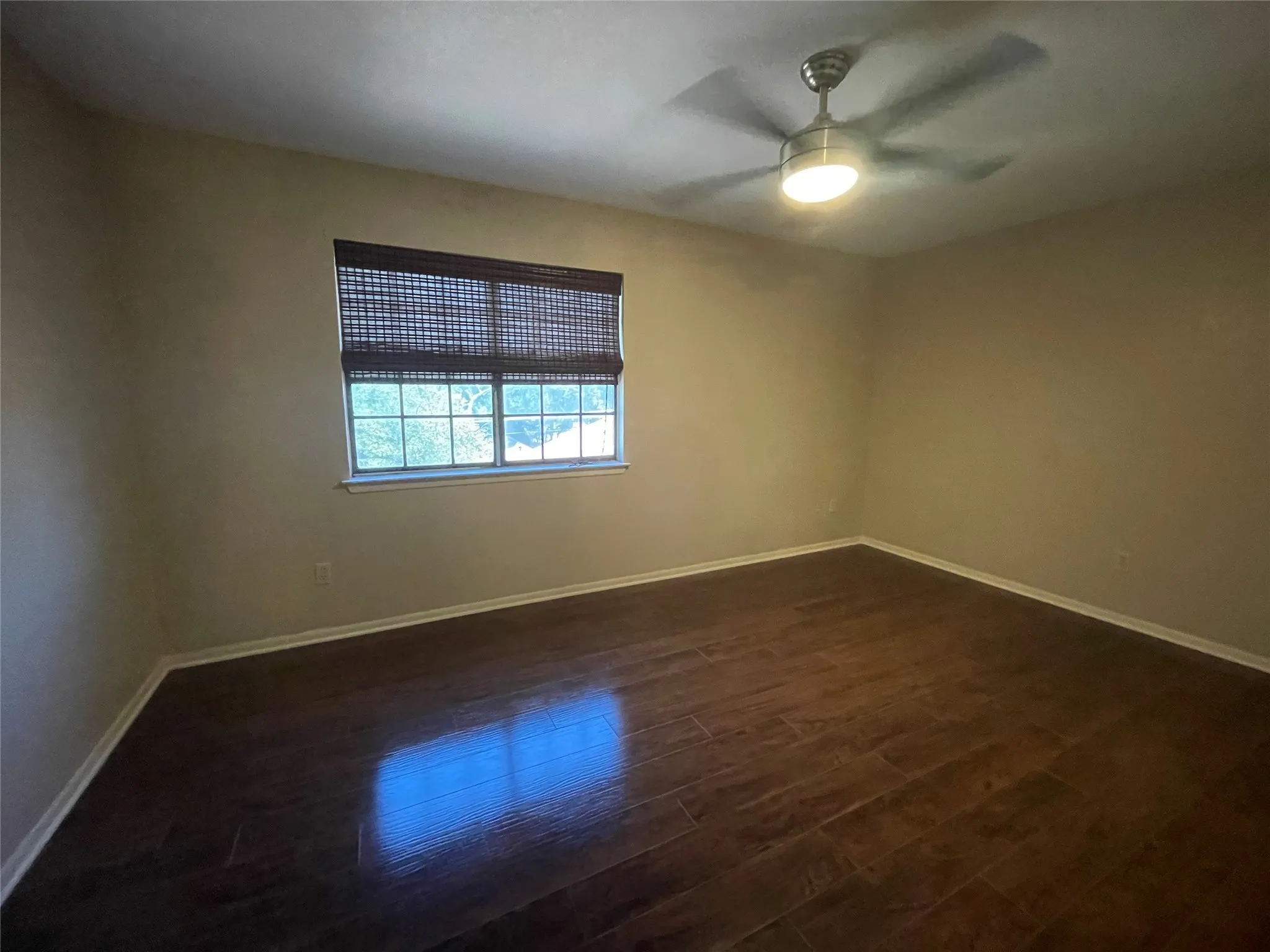Empty room with dark wood-type flooring, baseboards, and a ceiling fan