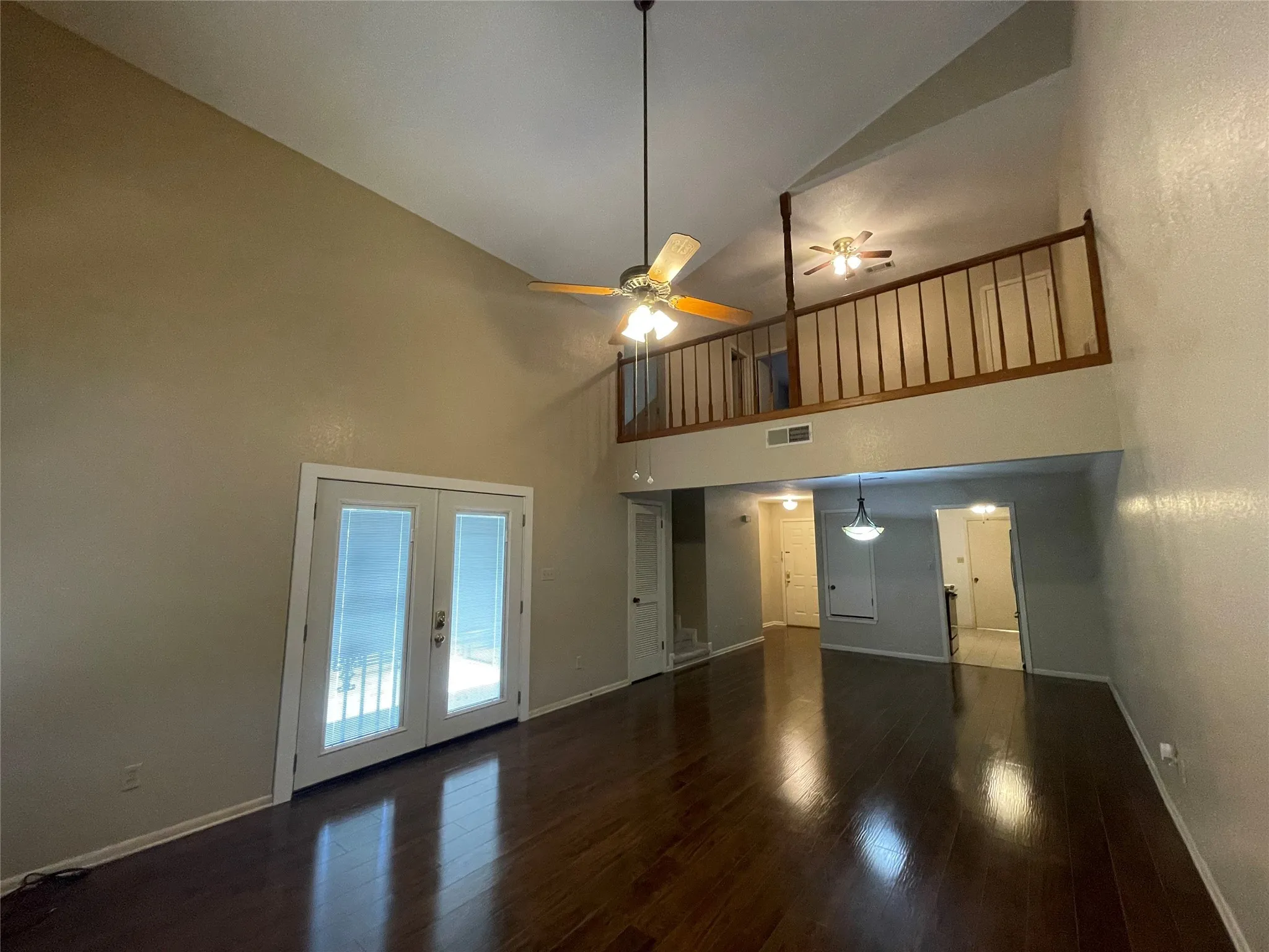 Unfurnished living room featuring high vaulted ceiling, baseboards, wood finished floors, french doors, and ceiling fan