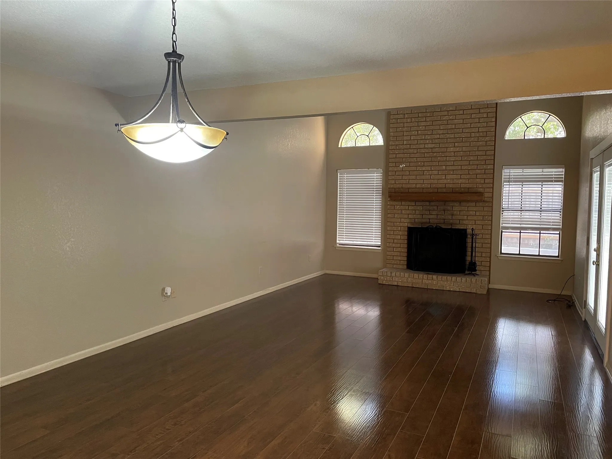 Unfurnished living room with healthy amount of natural light, baseboards, a brick fireplace, and dark wood-style flooring