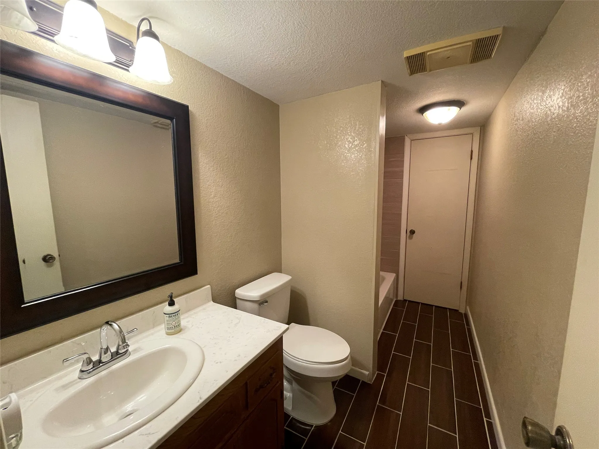 Bathroom with a textured wall, toilet, a textured ceiling, and vanity