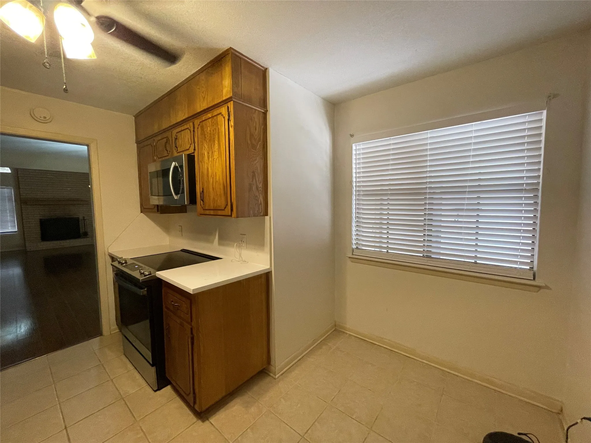 Kitchen featuring range with electric stovetop, stainless steel microwave, light countertops, brown cabinetry, and light tile patterned floors