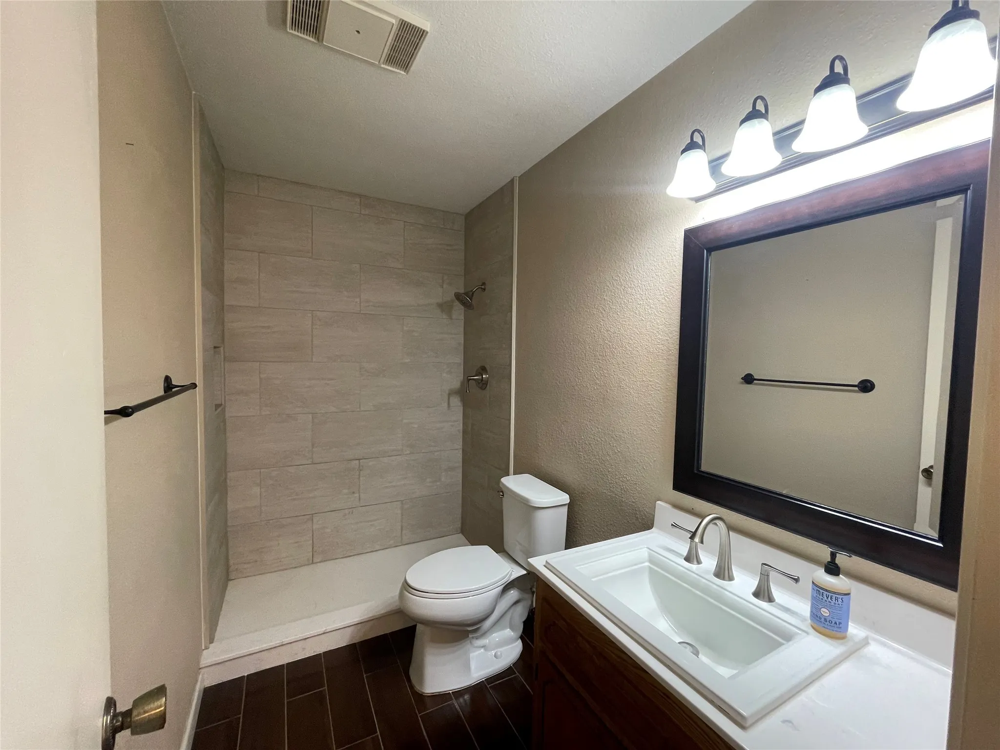 Full bath featuring toilet, tiled shower, vanity, and wood finished floors