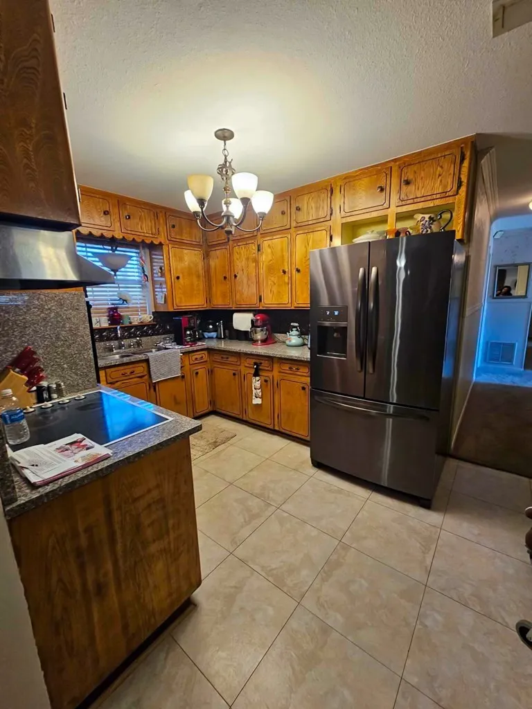 Kitchen featuring stainless steel fridge, brown cabinetry, a chandelier, a textured ceiling, and light tile patterned floors