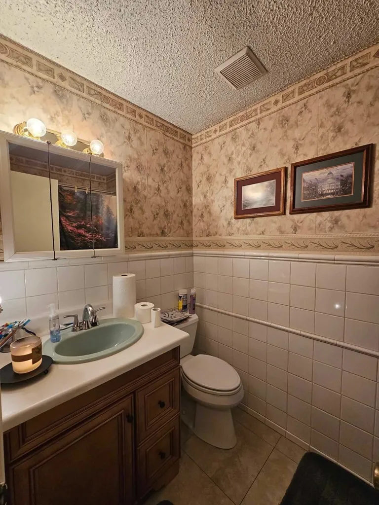 Bathroom with wallpapered walls, toilet, wainscoting, tile walls, and vanity