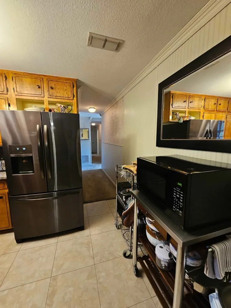 Kitchen with stainless steel refrigerator with ice dispenser, black microwave, crown molding, brown cabinets, and light tile patterned flooring
