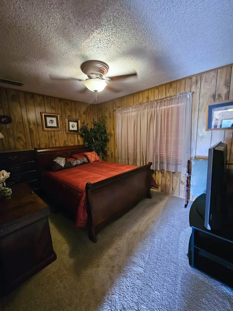 Bedroom featuring wooden walls, a textured ceiling, carpet, and ceiling fan