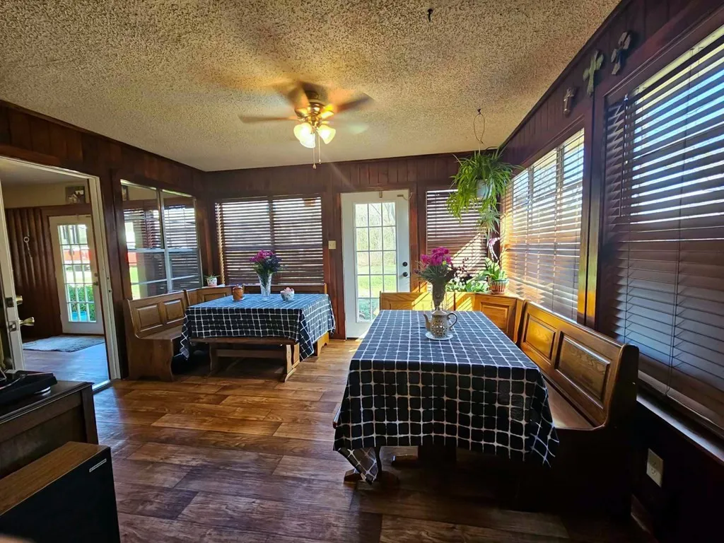 Dining room with a textured ceiling, ceiling fan, wood finished floors, and wood walls
