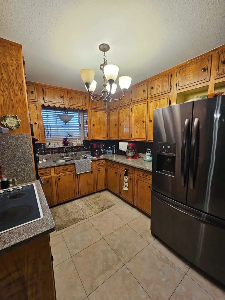 Kitchen with black appliances, brown cabinets, a chandelier, a textured ceiling, and light tile patterned floors