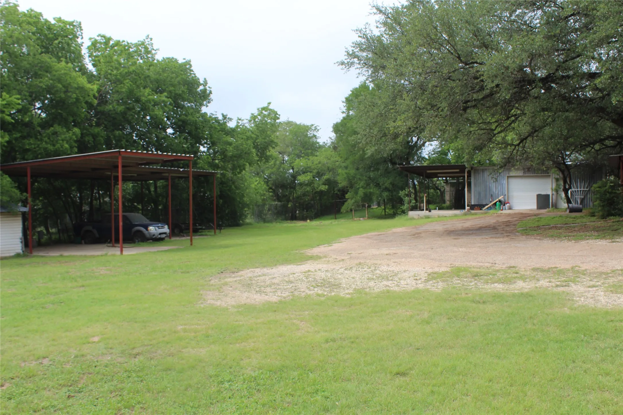 Expansive grassy area featuring a metal carport and a separate structure with a white roll-up garage door