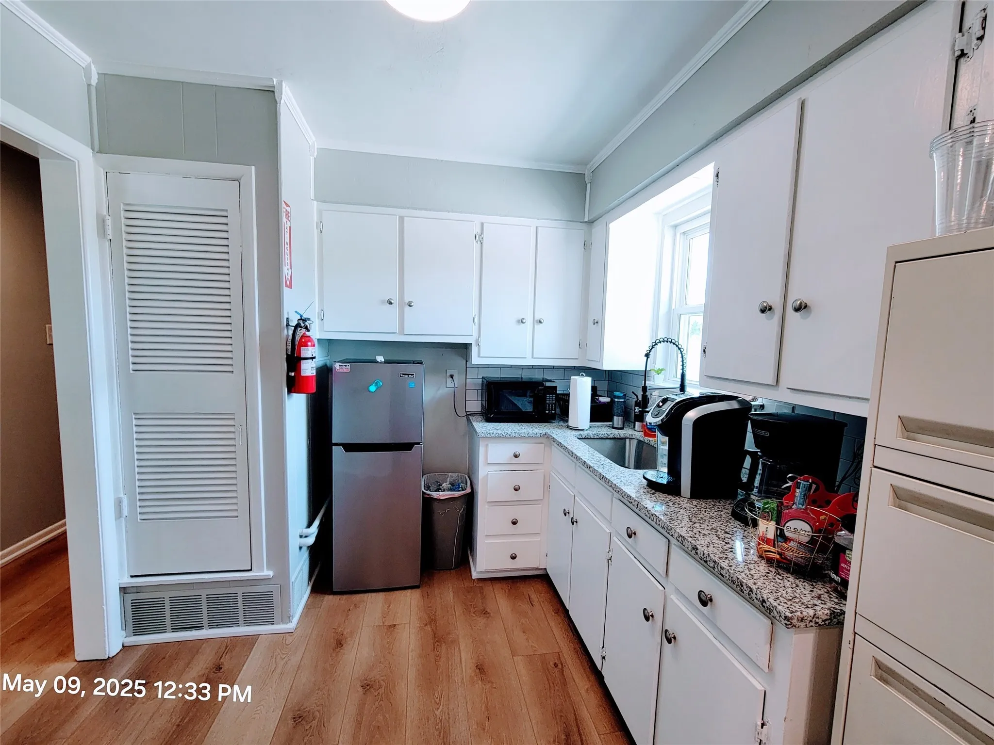 Kitchen with freestanding refrigerator, black microwave, a sink, light wood-style flooring, and ornamental molding