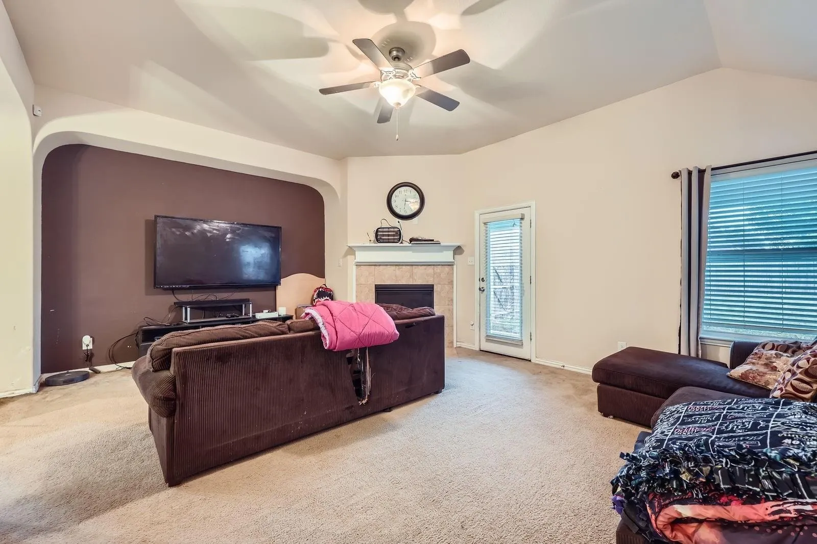 Carpeted living area with a ceiling fan, vaulted ceiling, a fireplace, and baseboards