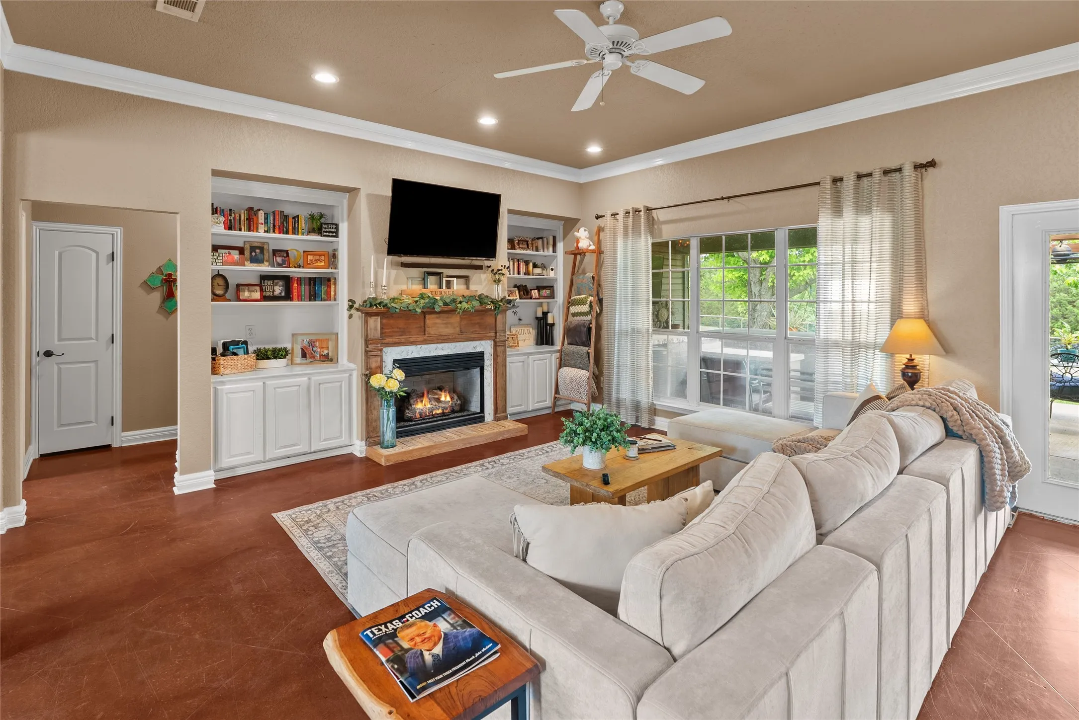 Living room featuring crown molding, a glass covered fireplace, a ceiling fan, baseboards, and built in features