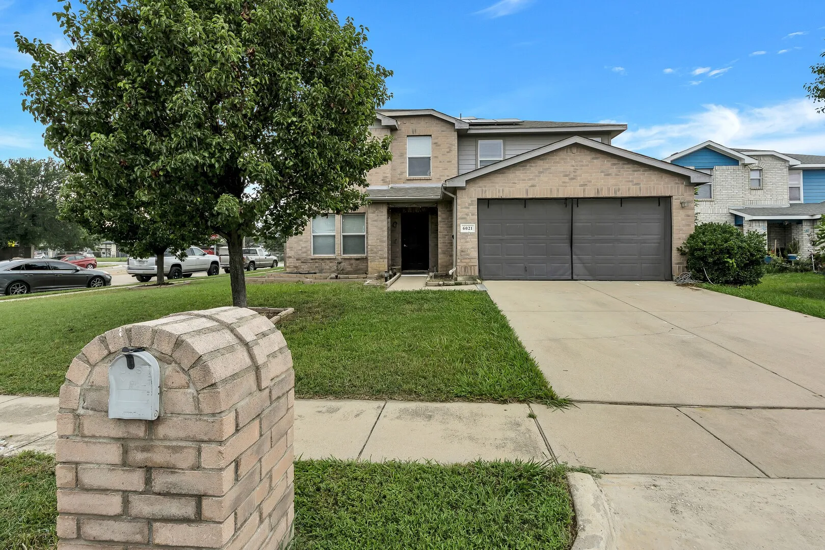 View of front of property with an attached garage, a front yard, solar panels, concrete driveway, and brick siding