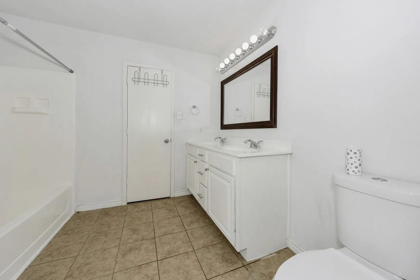 Full bath with toilet, tile patterned flooring, double vanity, baseboards, and washtub / shower combination