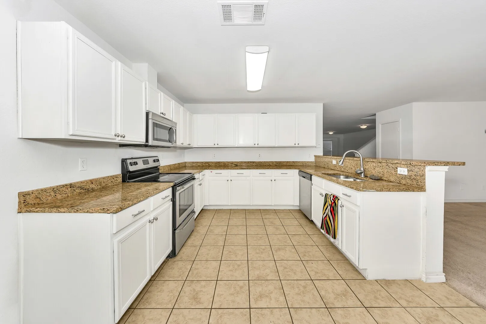 Kitchen featuring stainless steel appliances, a sink, a peninsula, light tile patterned floors, and stone countertops