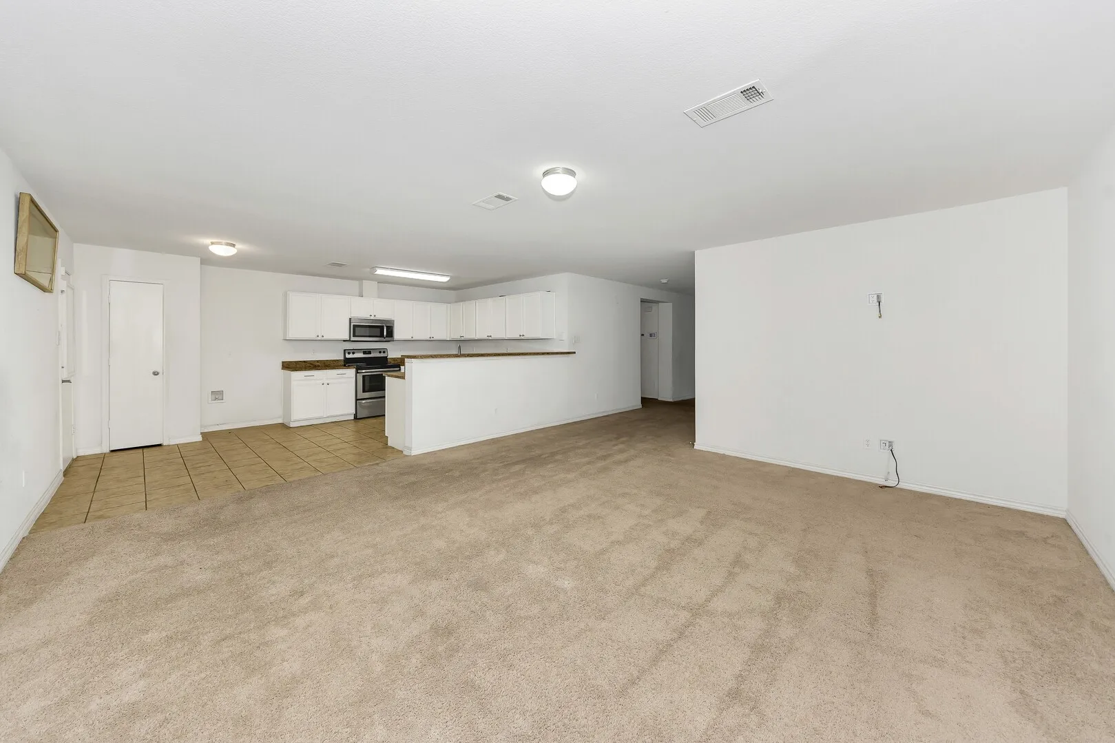 Unfurnished living room with light colored carpet, light tile patterned flooring, and baseboards