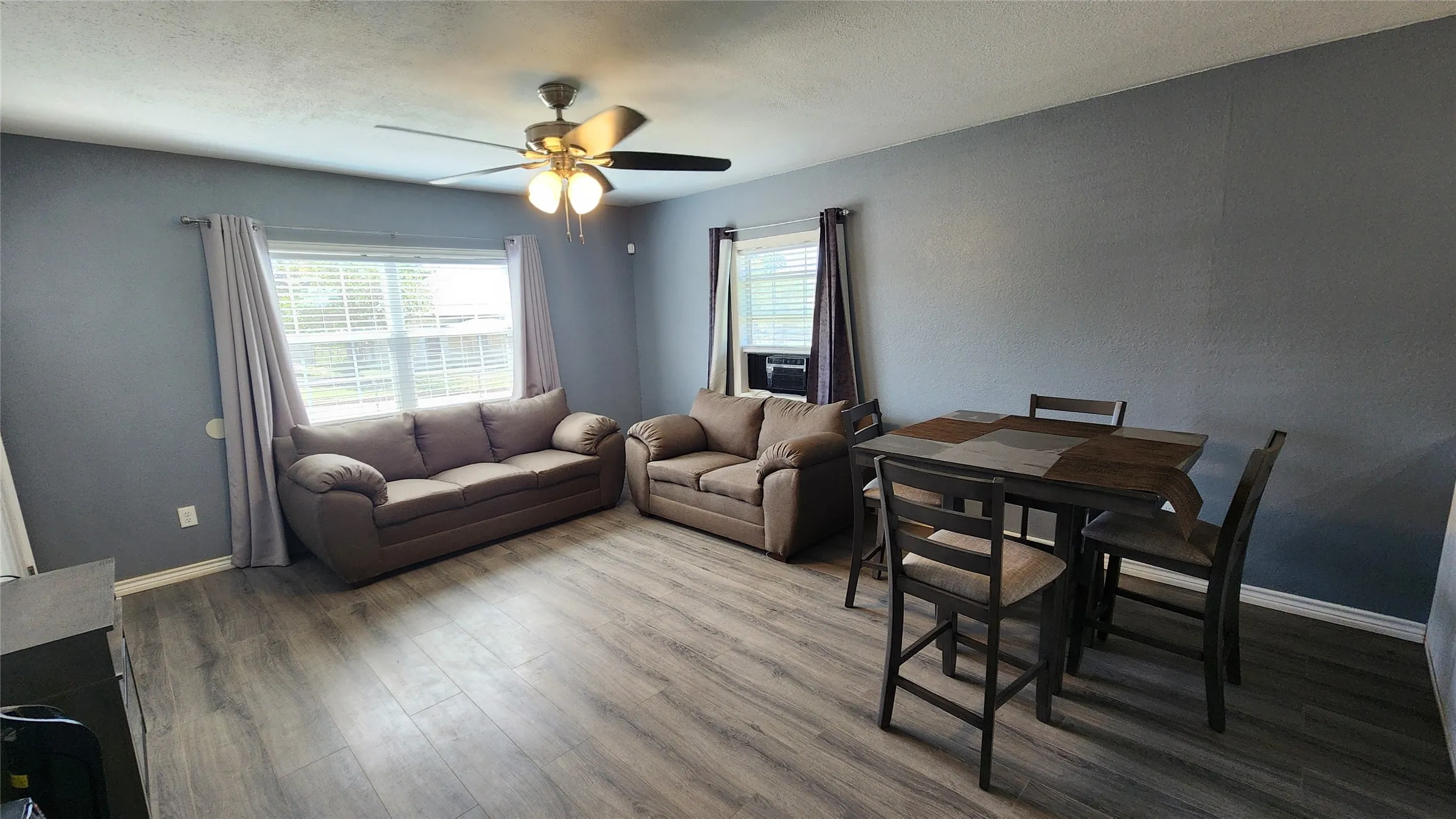 Living room with ceiling fan, wood finished floors, baseboards, and cooling unit