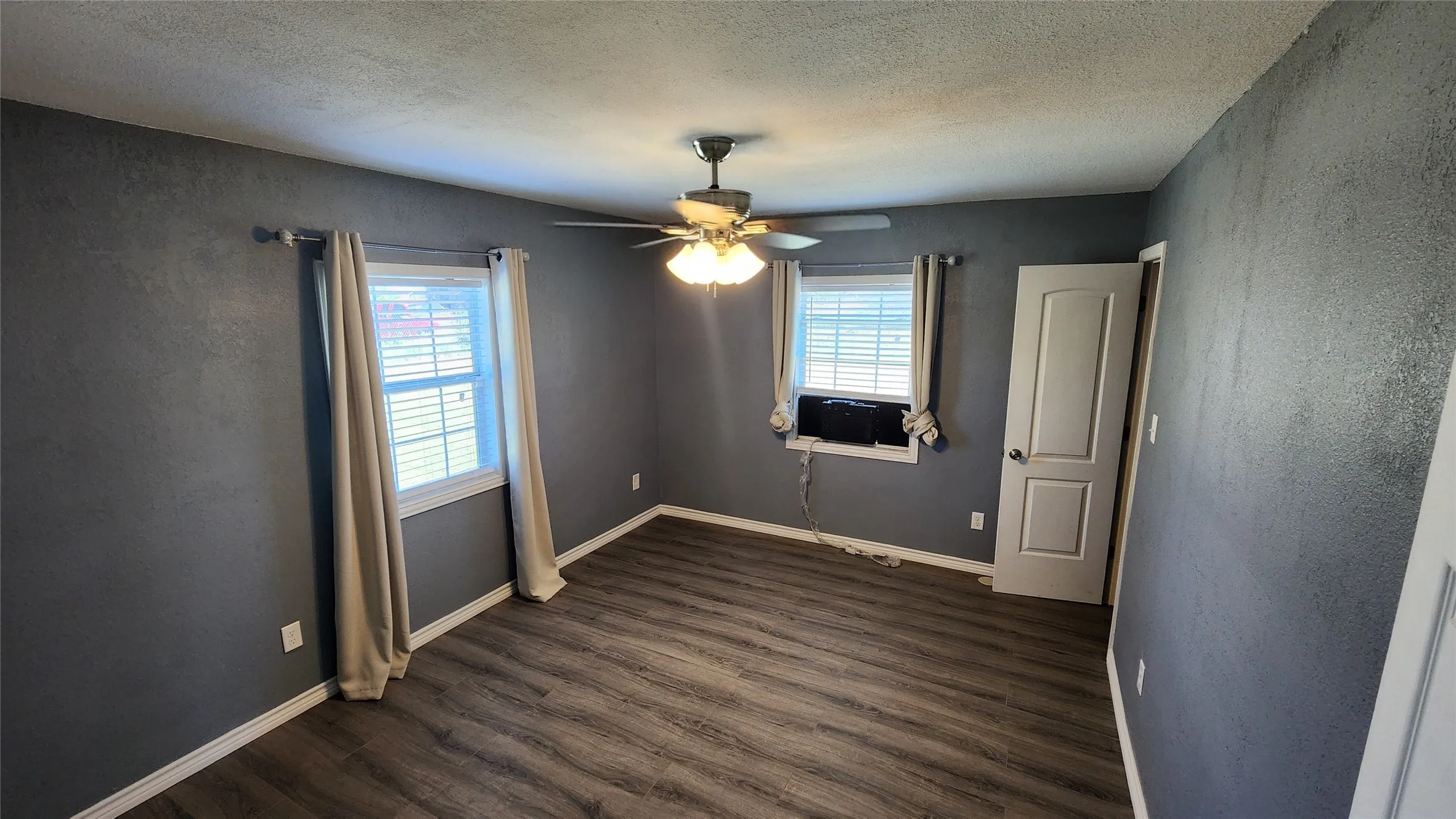 Spare room with dark wood-style floors, ceiling fan, a textured ceiling, cooling unit, and baseboards
