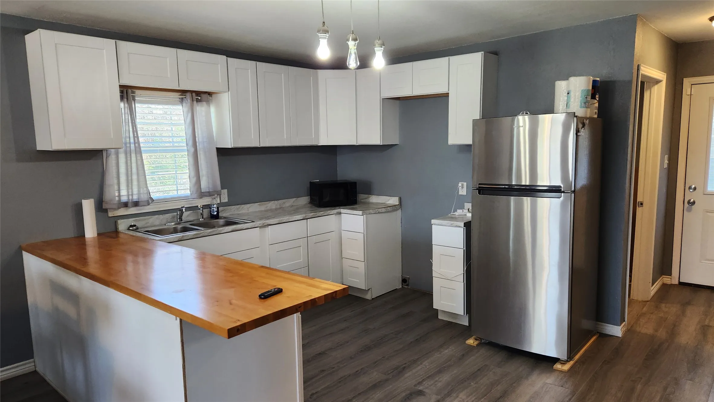 Kitchen featuring freestanding refrigerator, wood counters, a sink, dark wood-type flooring, and black microwave