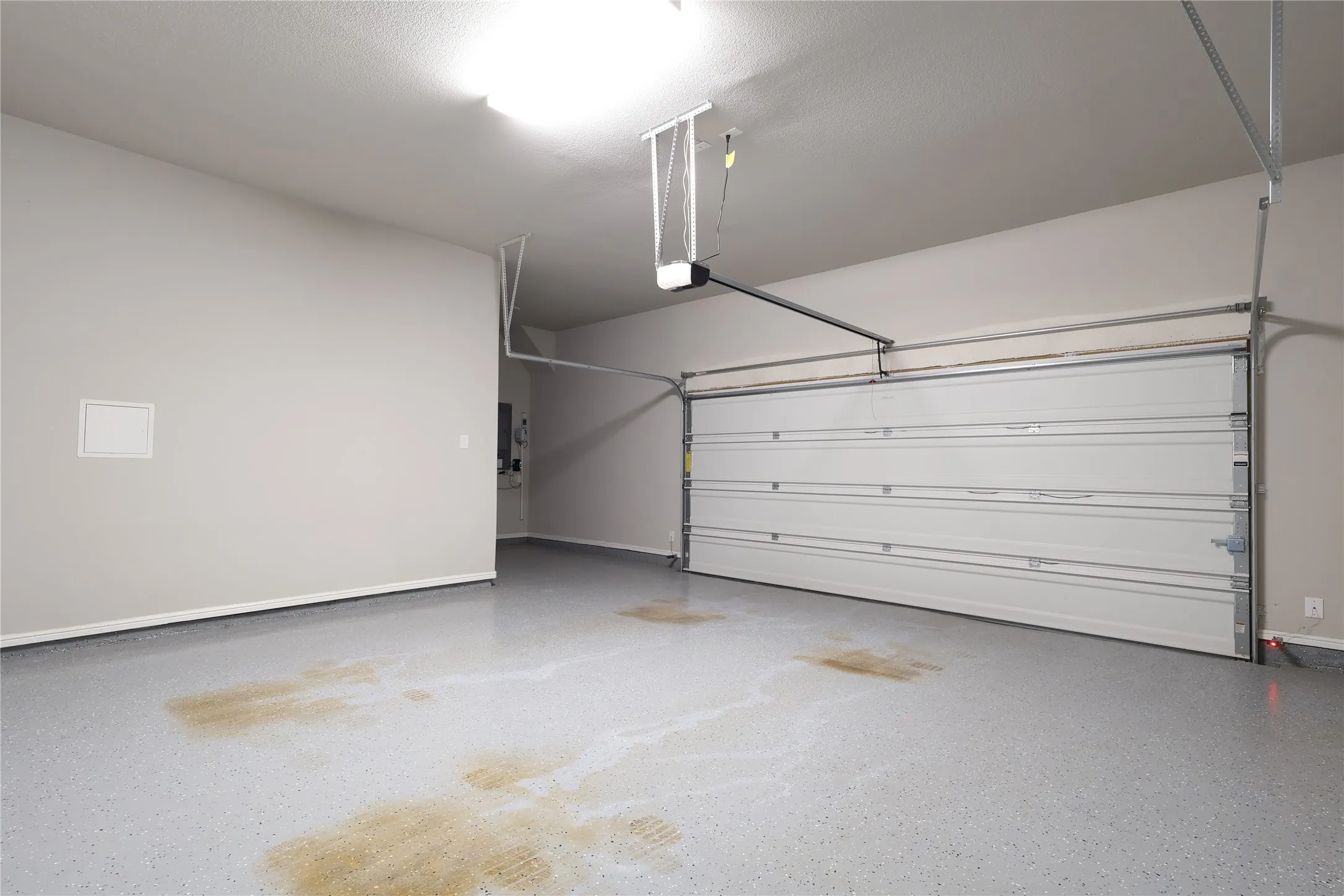 Garage with a garage door opener, electric panel, and baseboards