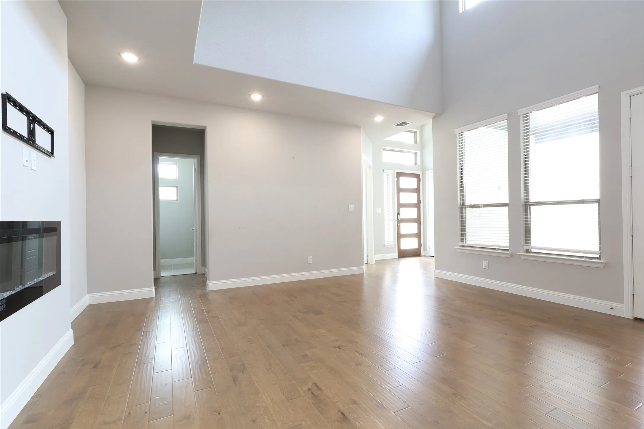 Unfurnished living room featuring recessed lighting, wood finished floors, baseboards, and a towering ceiling