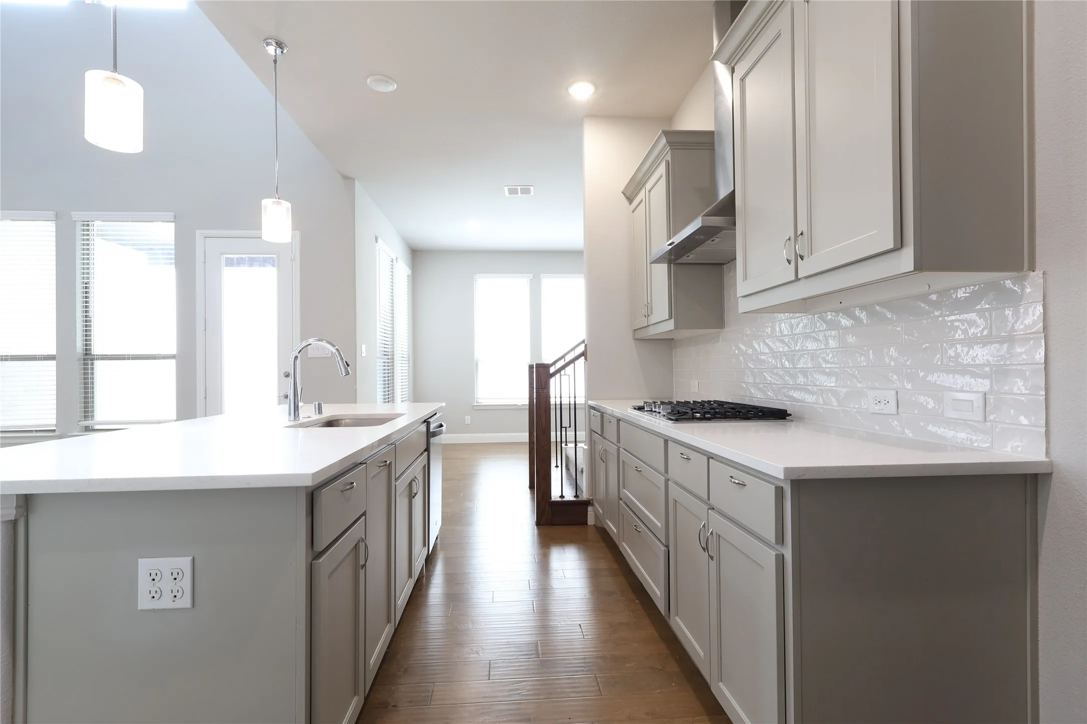 Kitchen with dark wood-type flooring, gray cabinetry, backsplash, stainless steel gas stovetop, and a sink