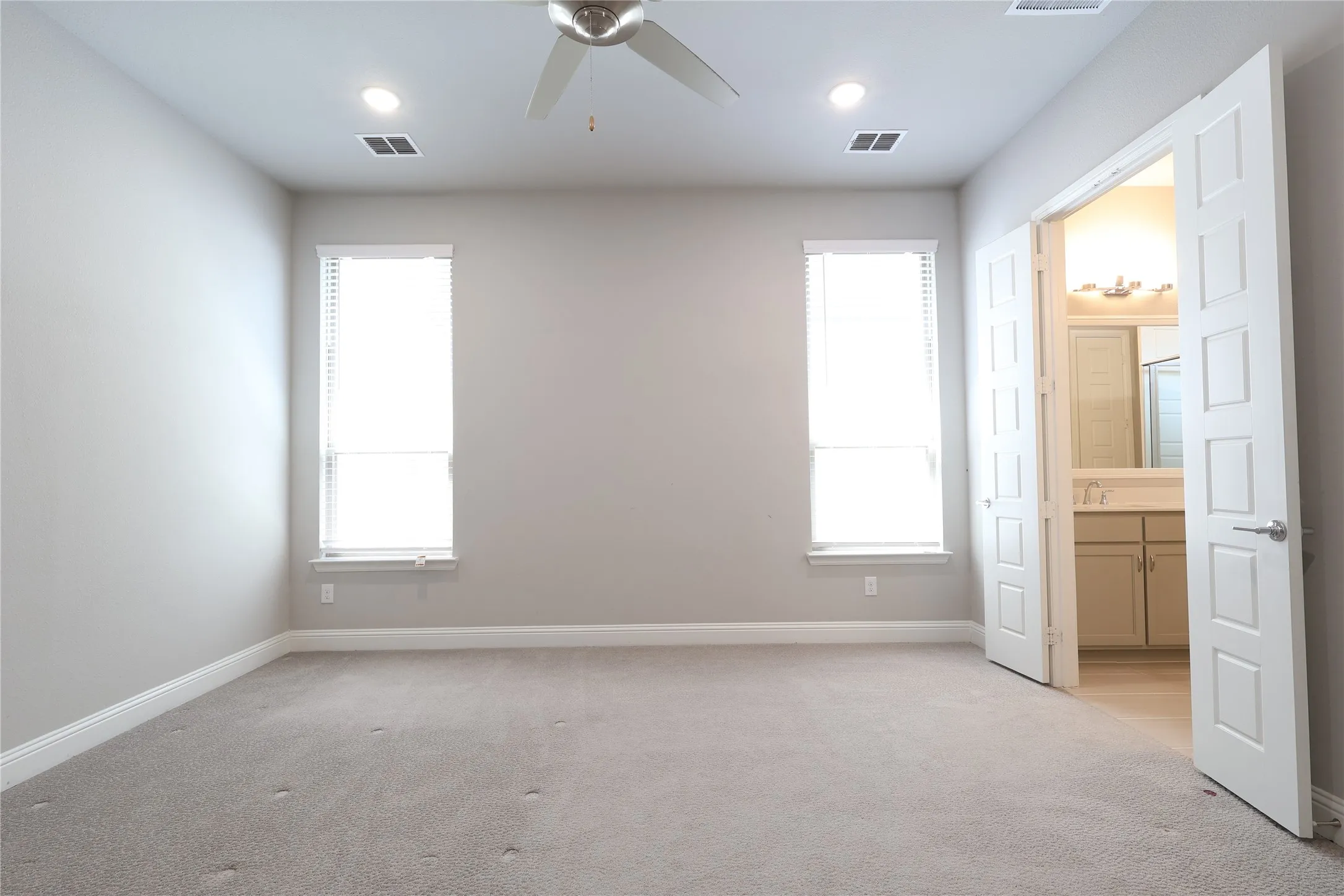 Unfurnished bedroom with light colored carpet, baseboards, ensuite bathroom, and recessed lighting
