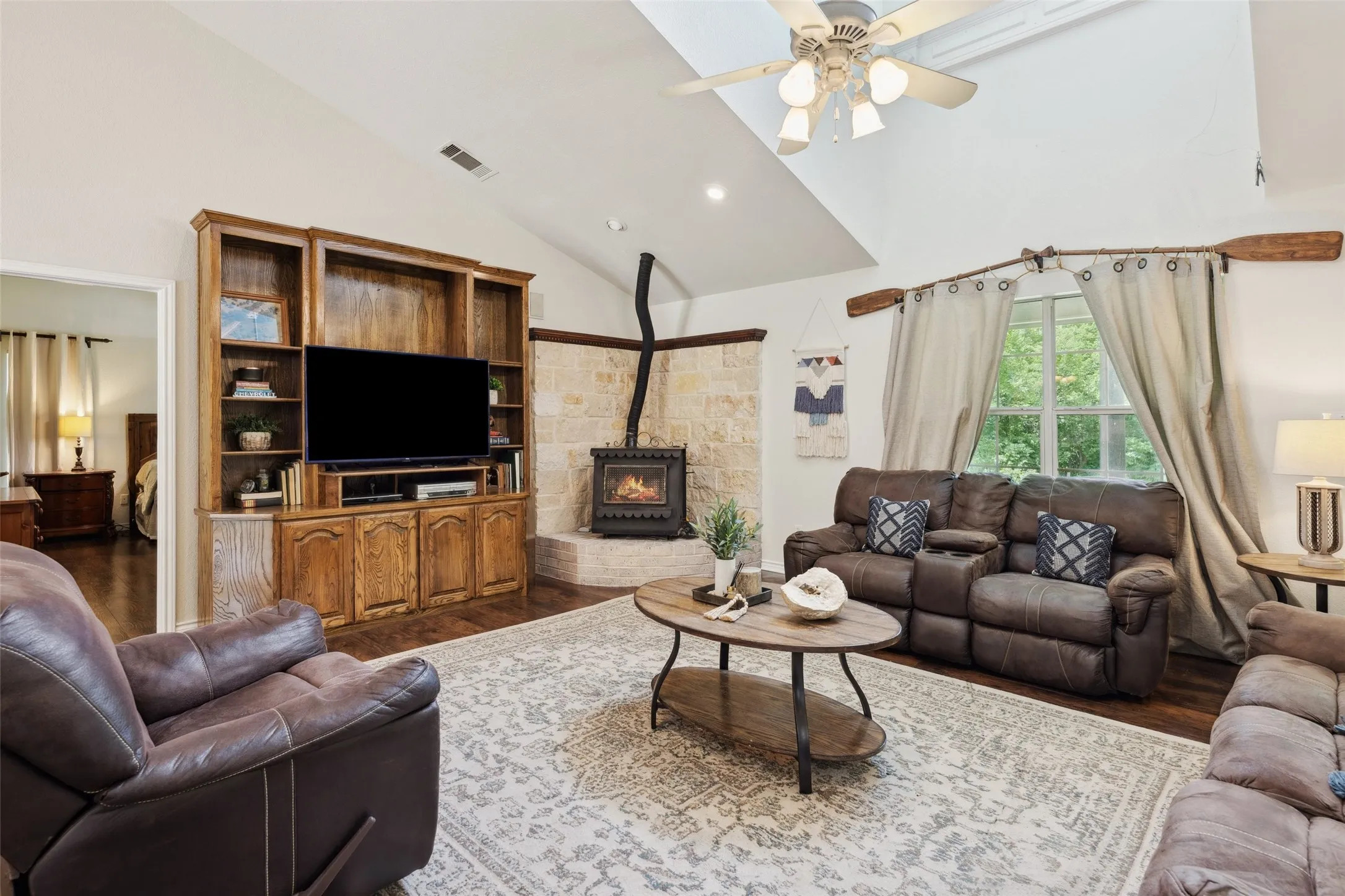Light-filled living room with soaring ceilings, a grand window, cozy stove fireplace, and built-in media center—perfect for relaxed gatherings