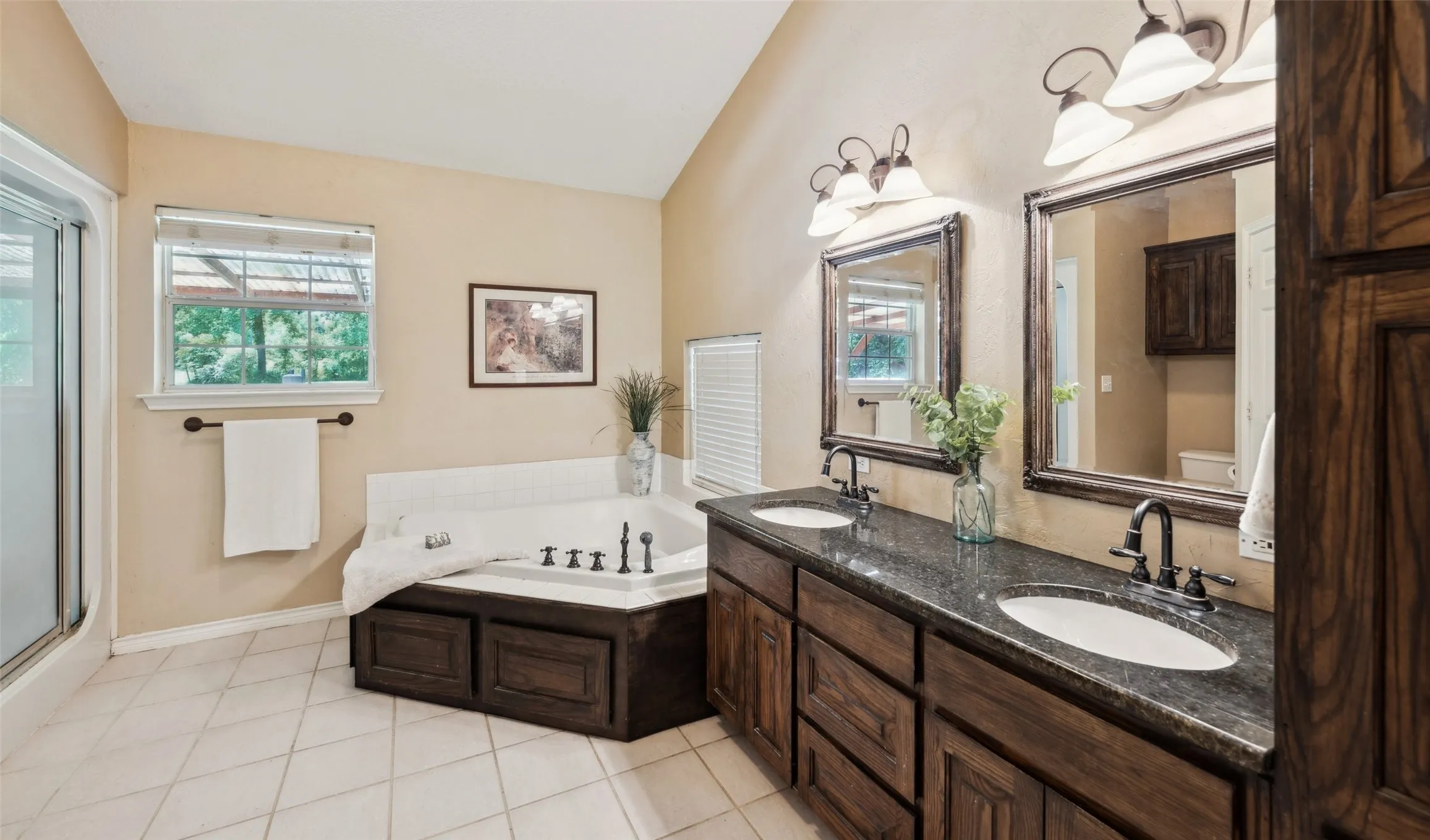 Jetted tub and separate glass-enclosed shower, complemented by warm cabinetry with ample storage and an oversized primary closet.