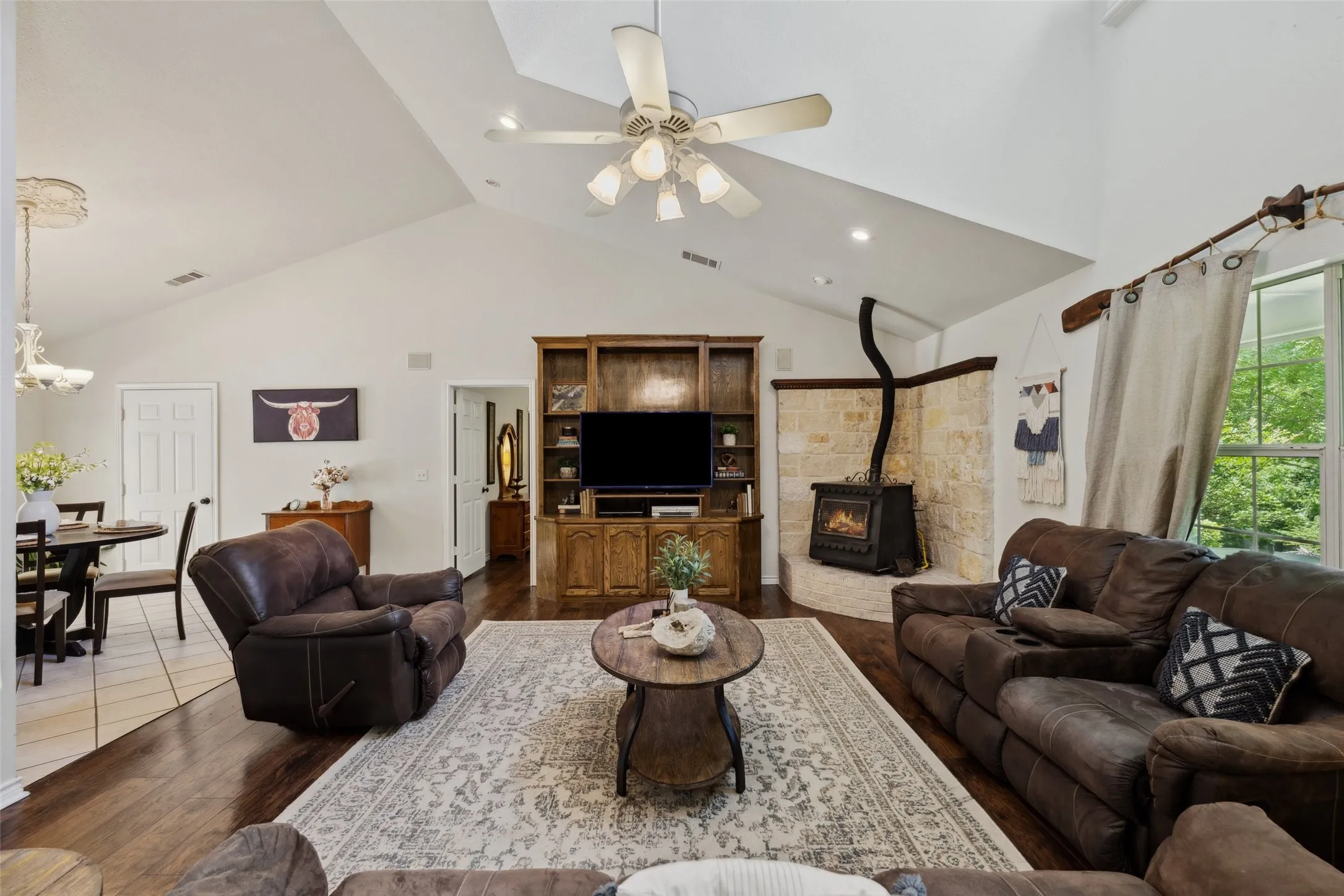 Light-filled living room with soaring ceilings, a grand window, cozy stove fireplace, and built-in media center—perfect for relaxed gatherings
