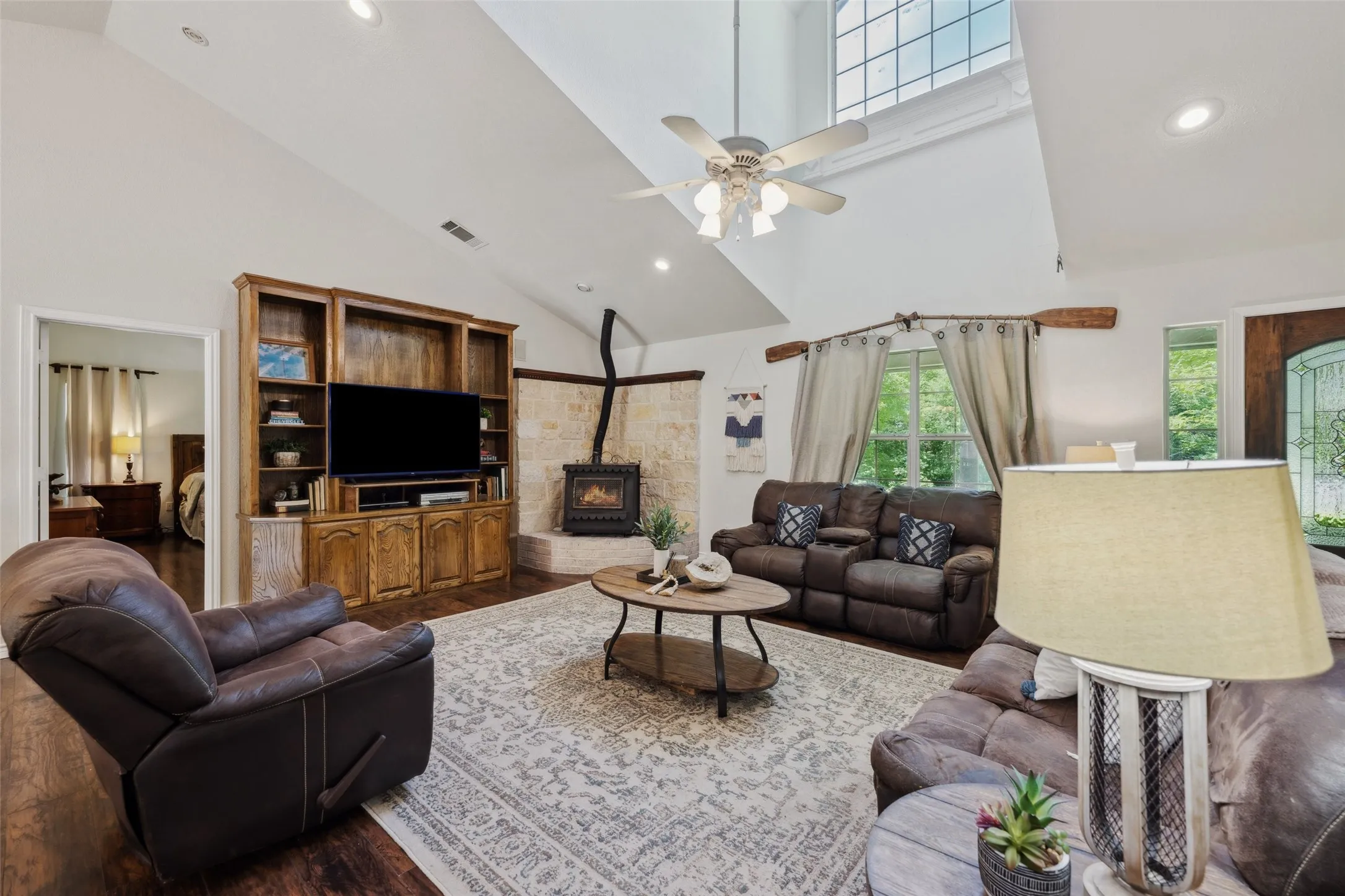 Light-filled living room with soaring ceilings, a grand window, cozy stove fireplace, and built-in media center—perfect for relaxed gatherings