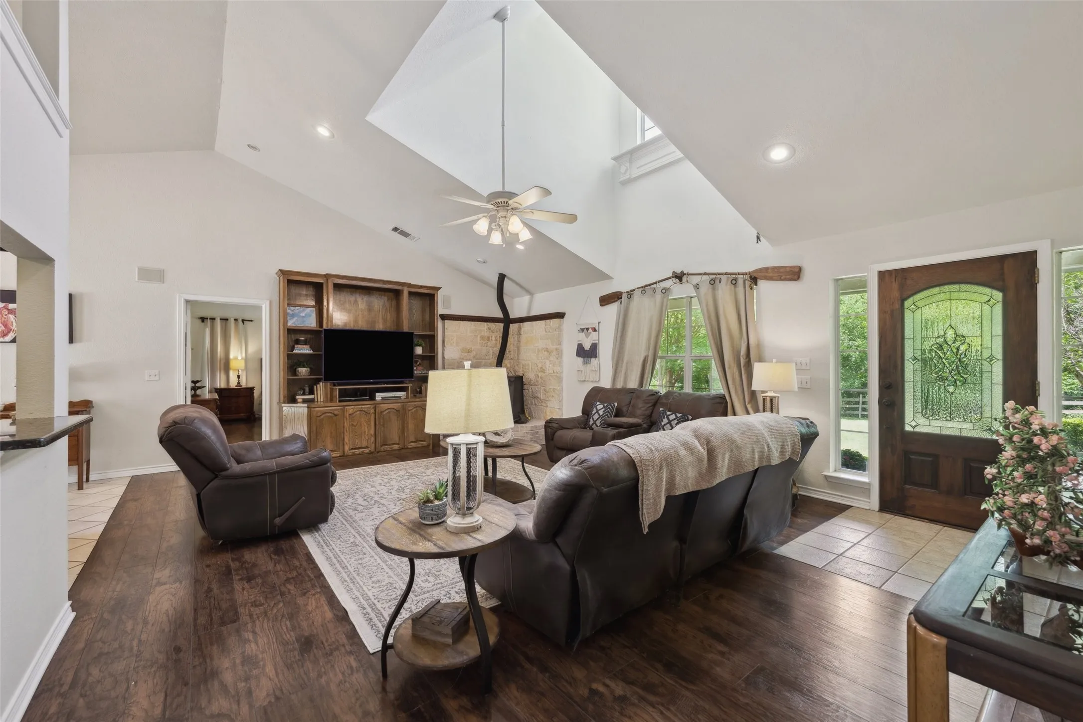 Light-filled living room with soaring ceilings, a grand window, cozy stove fireplace, and built-in media center—perfect for relaxed gatherings