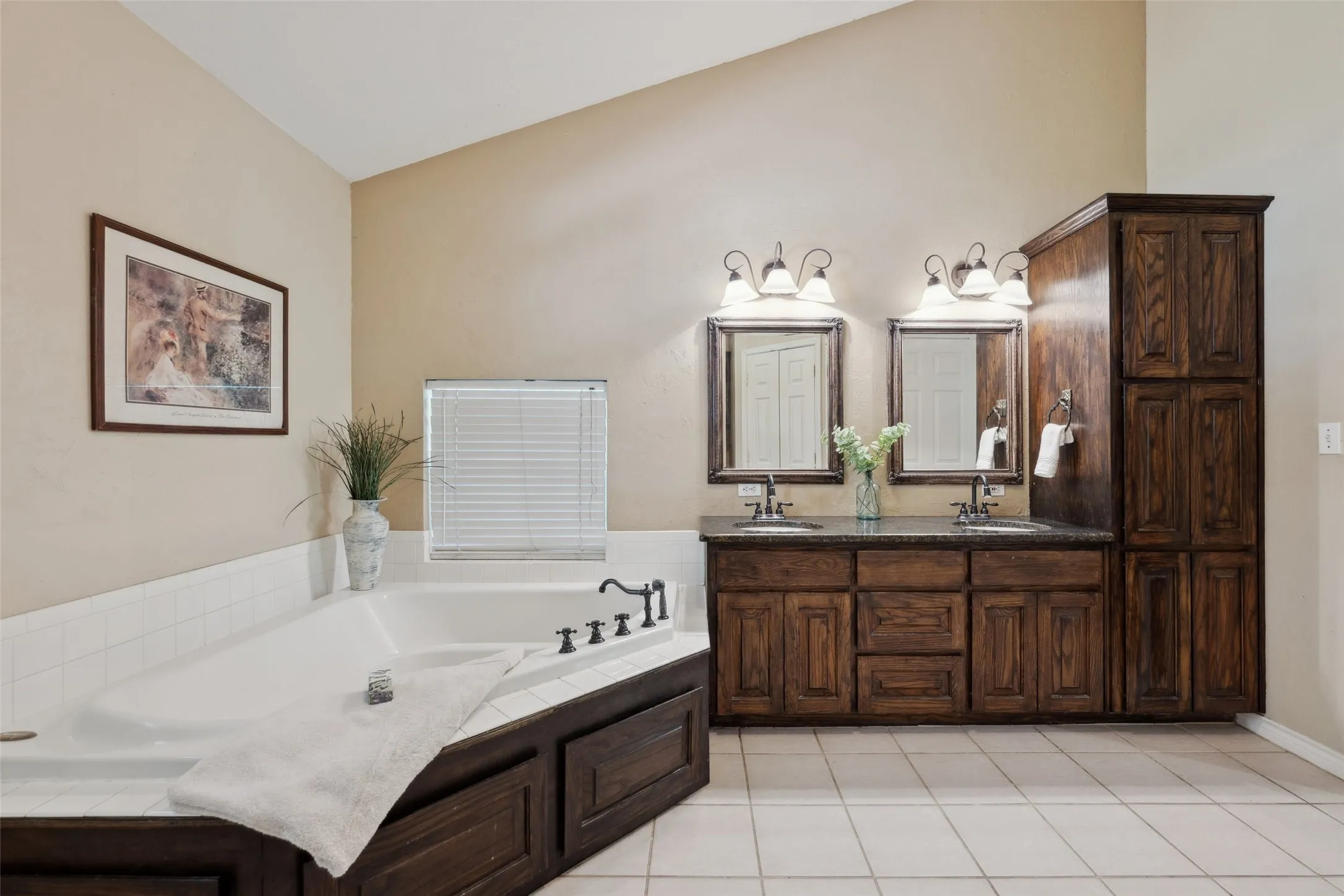 Jetted tub and separate glass-enclosed shower, complemented by warm cabinetry with ample storage and an oversized primary closet.