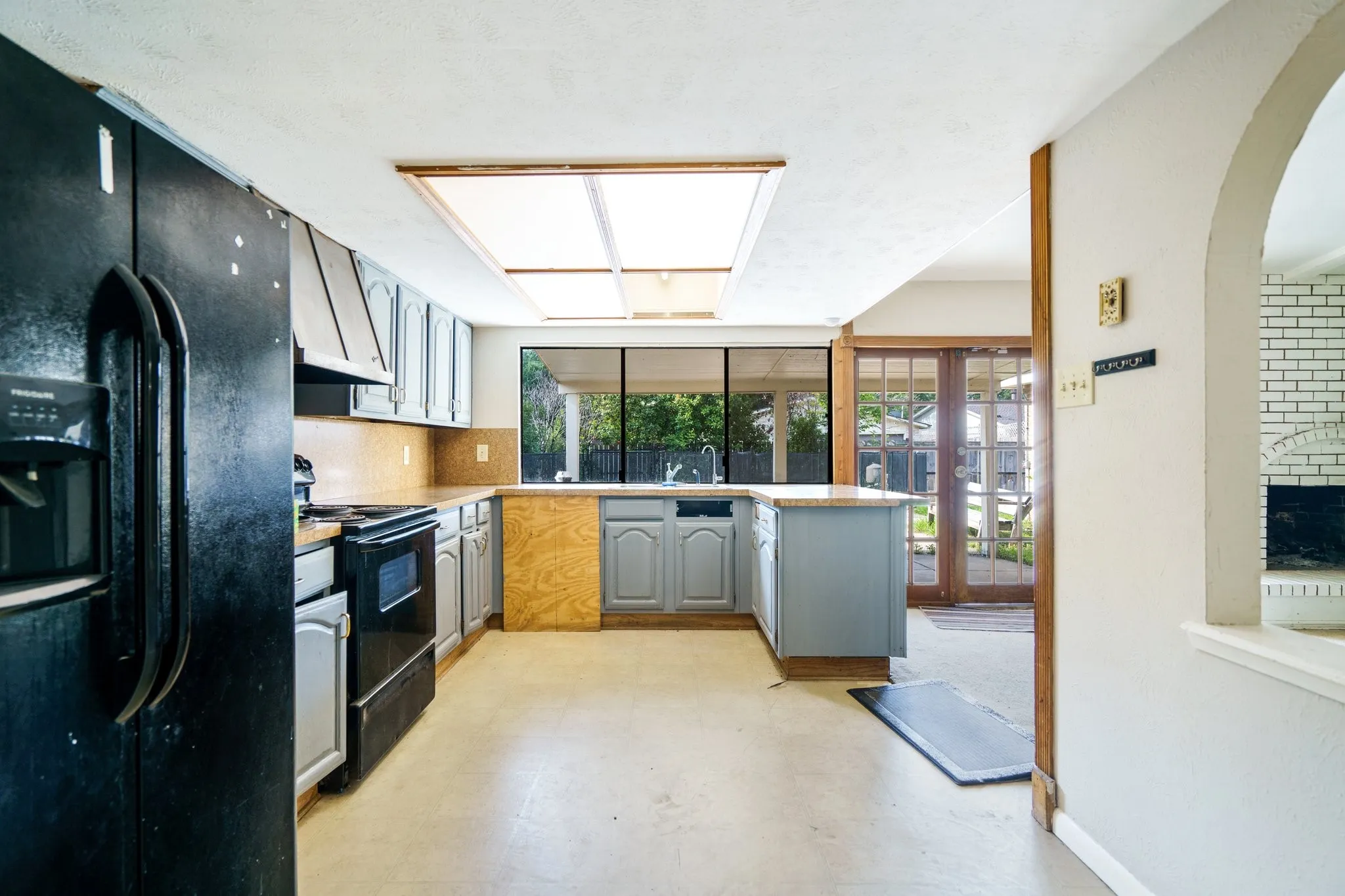 Kitchen featuring black appliances, gray cabinets, under cabinet range hood, light flooring, and arched walkways