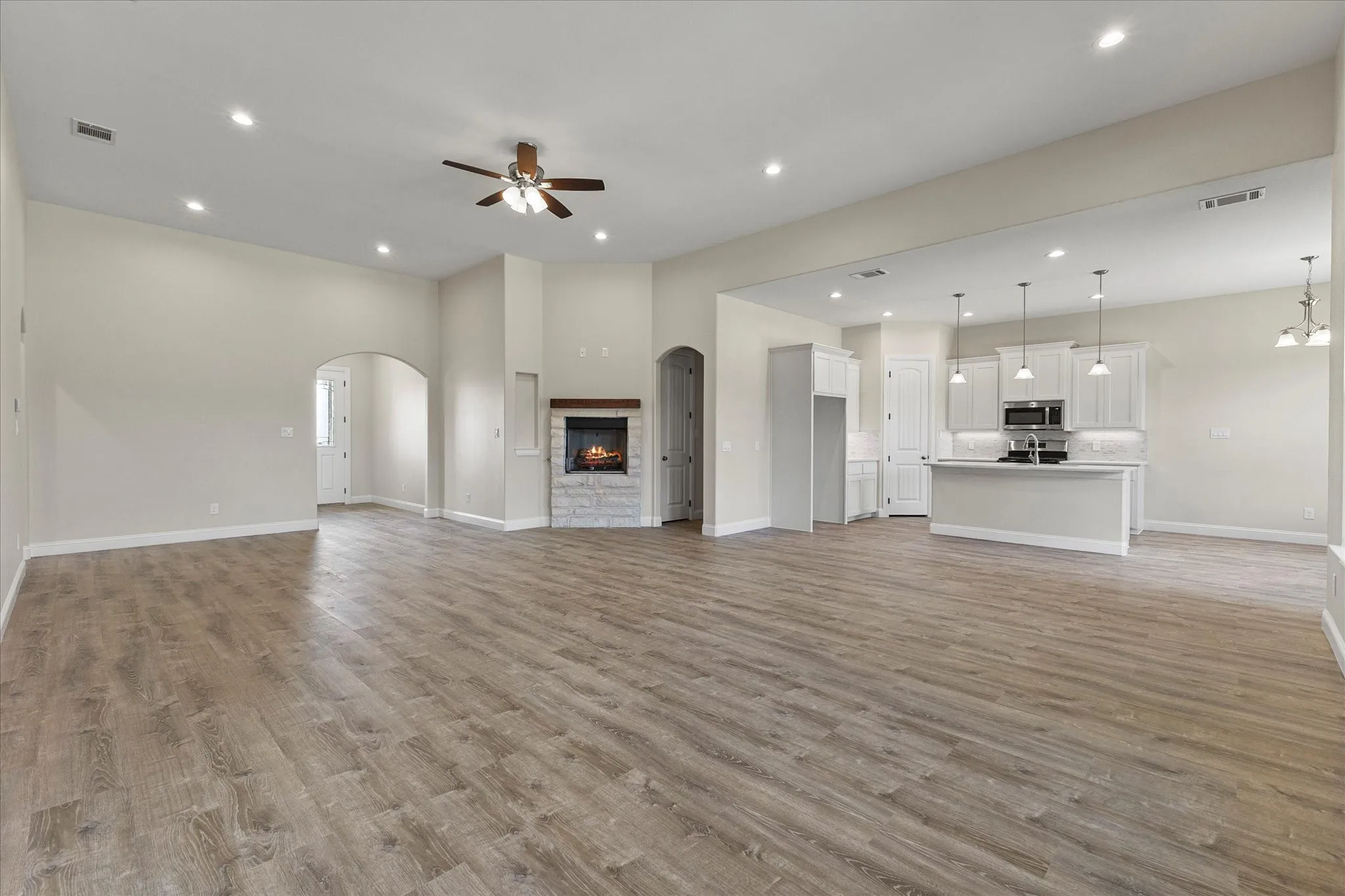Unfurnished living room with a ceiling fan, light wood-style flooring, recessed lighting, a stone fireplace, and arched walkways