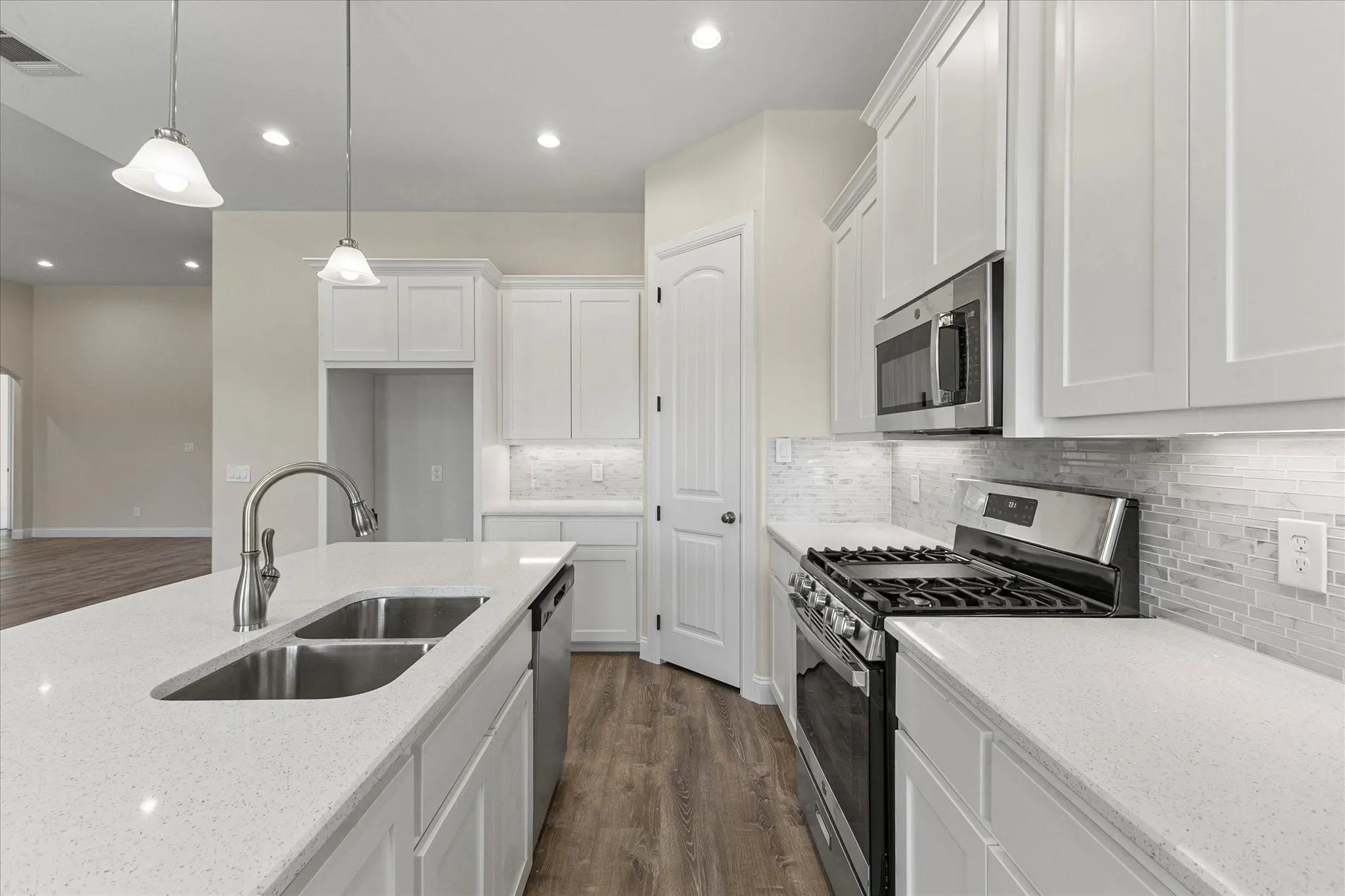 Kitchen with stainless steel appliances, dark wood-type flooring, white cabinets, light stone countertops, and backsplash
