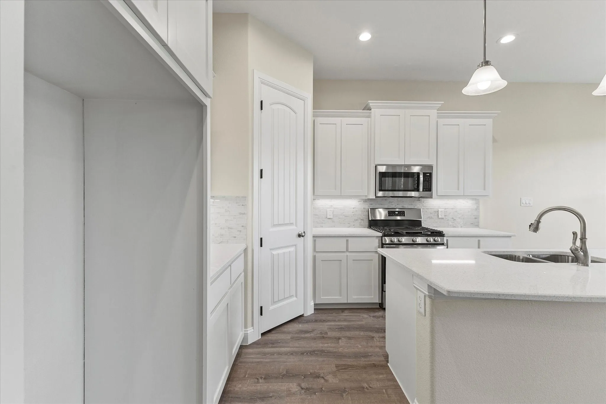 Kitchen with appliances with stainless steel finishes, backsplash, white cabinetry, dark wood-style flooring, and hanging light fixtures