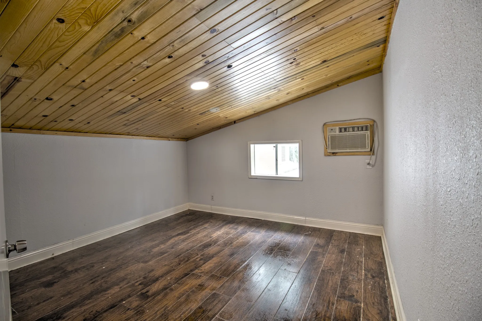 Additional living space featuring a wall unit AC, vaulted ceiling, baseboards, dark wood-type flooring, and wooden ceiling