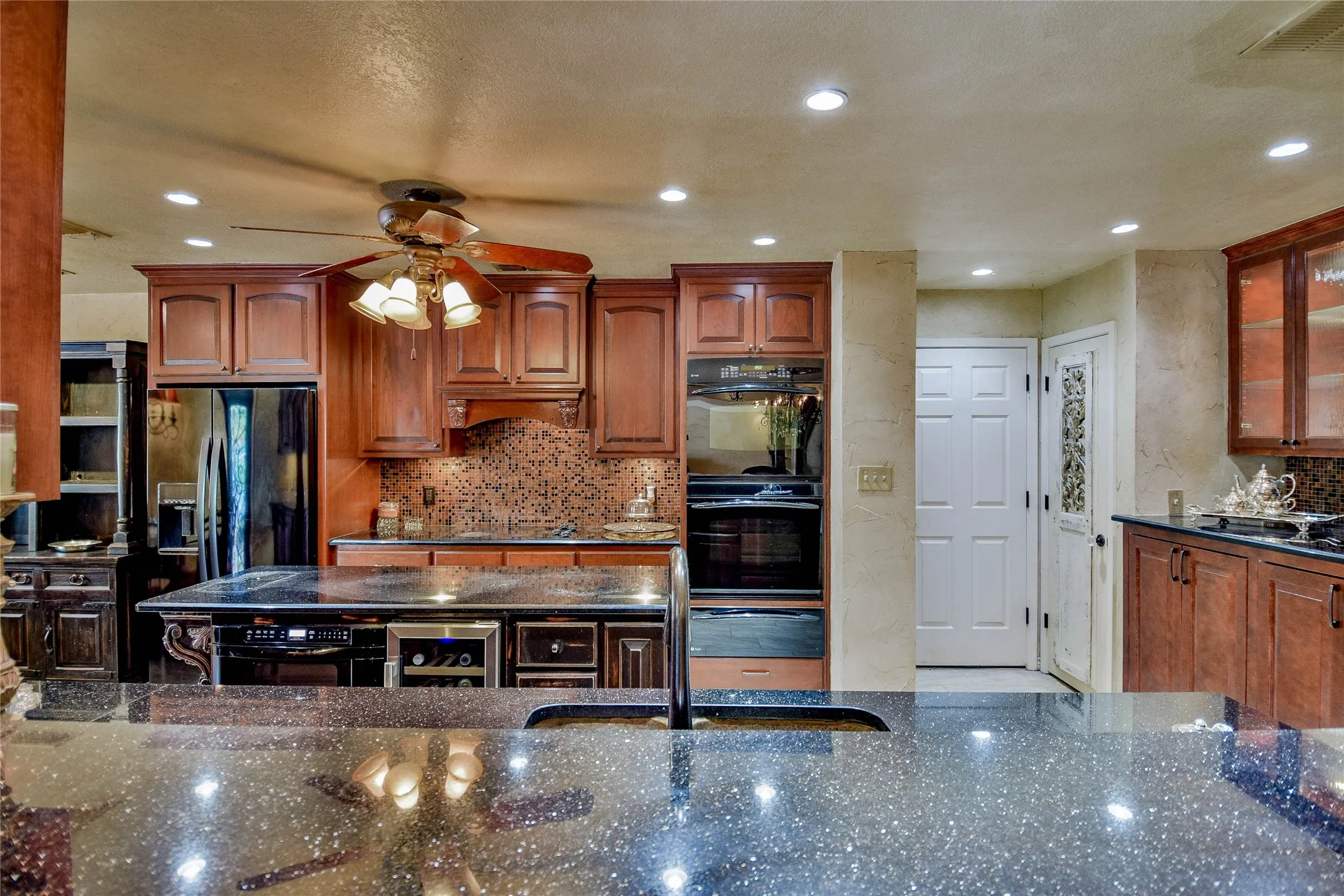 Kitchen featuring black appliances, a ceiling fan, dark stone countertops, beverage cooler, and backsplash