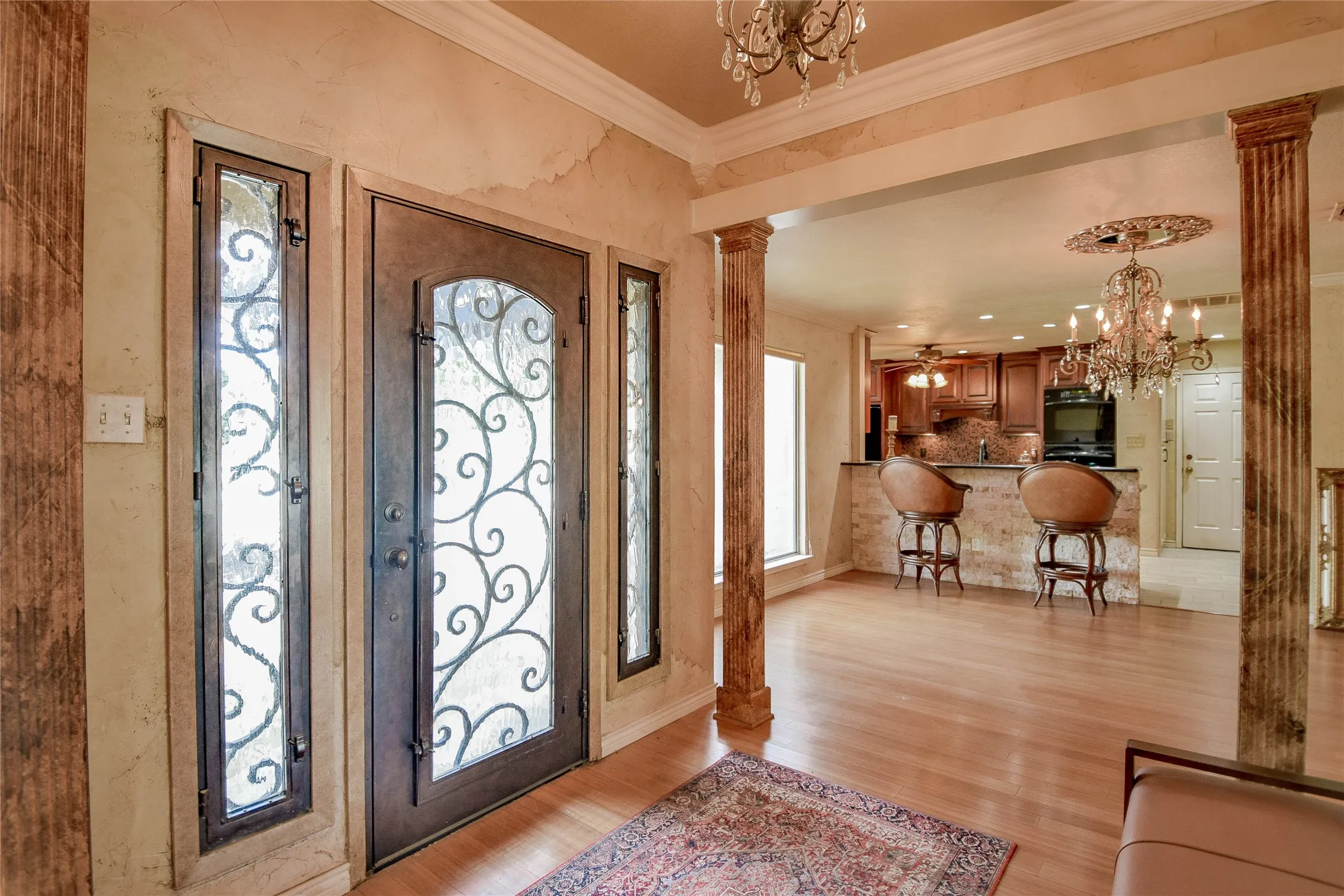 Foyer entrance with decorative columns, a chandelier, ornamental molding, and light wood finished floors