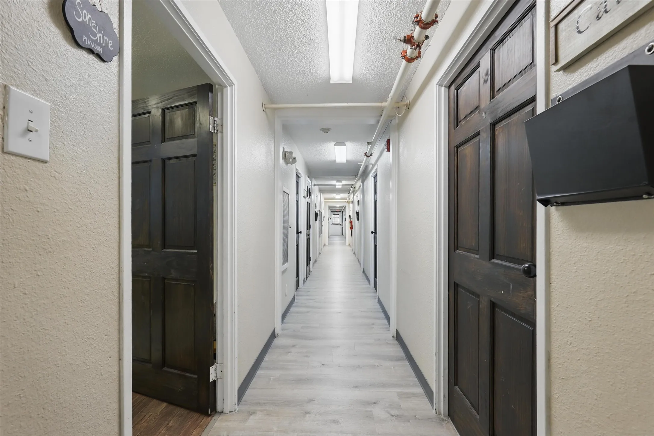 Hallway featuring light wood-style floors, a textured wall, and a textured ceiling