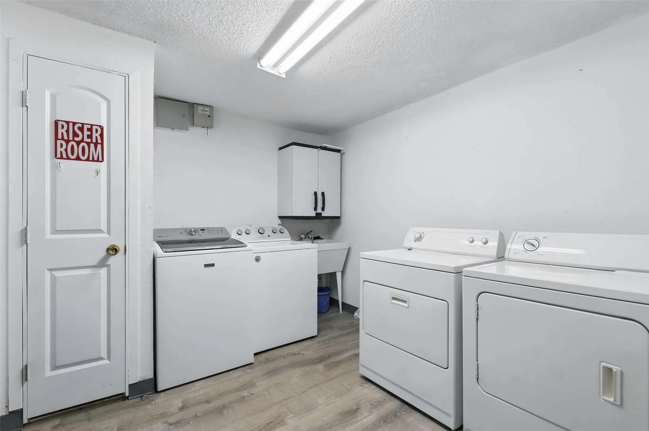 Laundry room with washer and clothes dryer, cabinet space, a textured ceiling, and light wood-type flooring