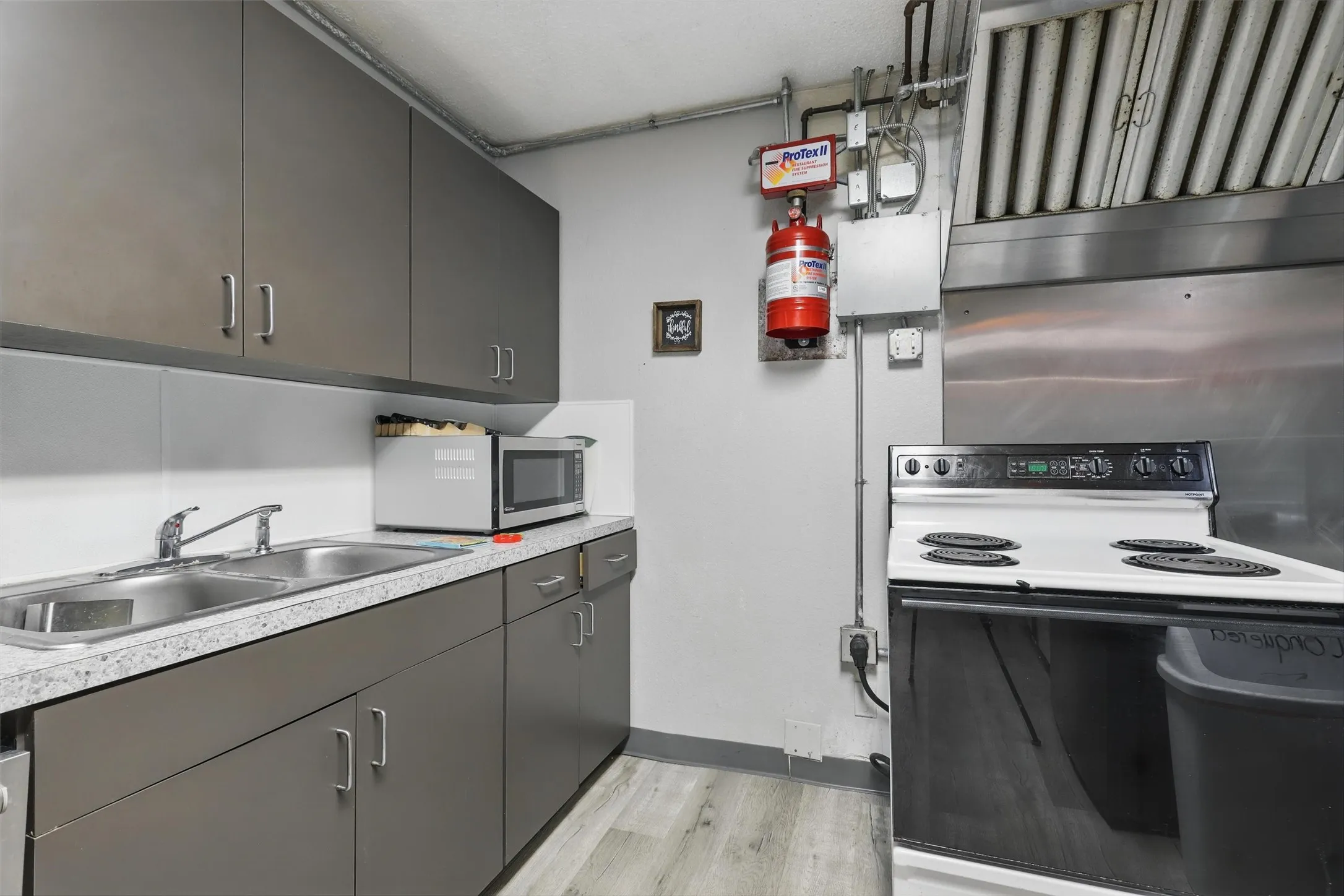 Kitchen featuring electric range, stainless steel microwave, a sink, light wood-type flooring, and light countertops