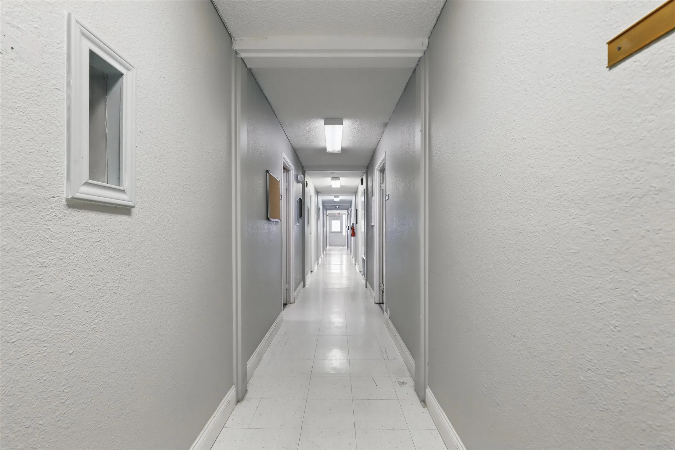 Corridor with a textured wall, light tile patterned floors, and baseboards