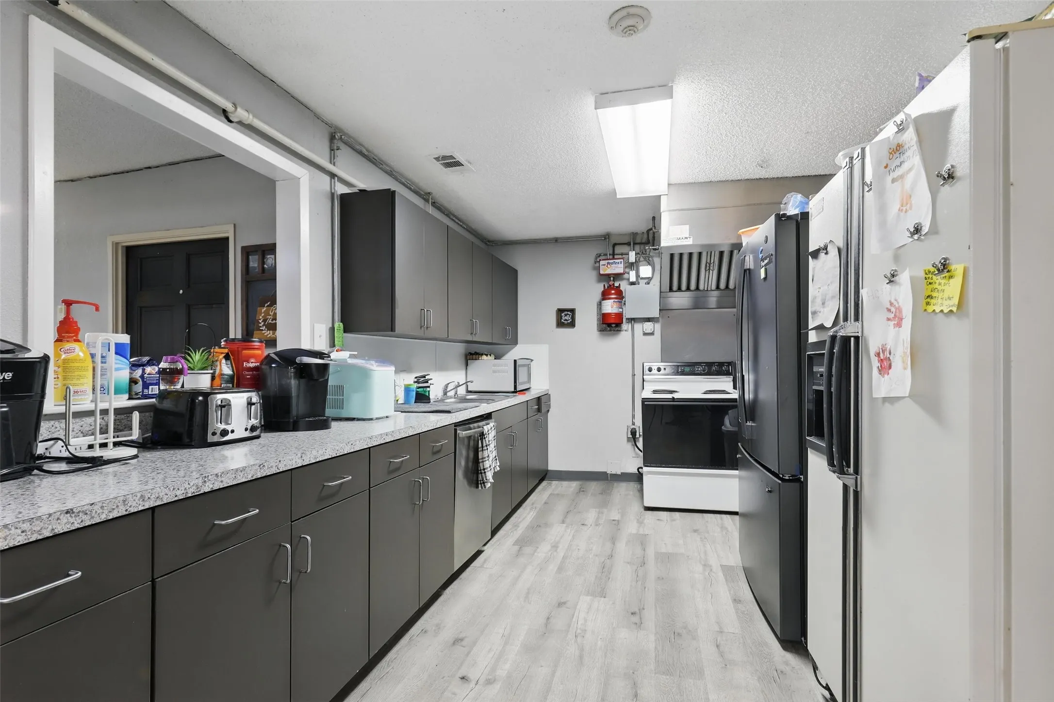 Kitchen with appliances with stainless steel finishes, light wood finished floors, light countertops, a sink, and a textured ceiling