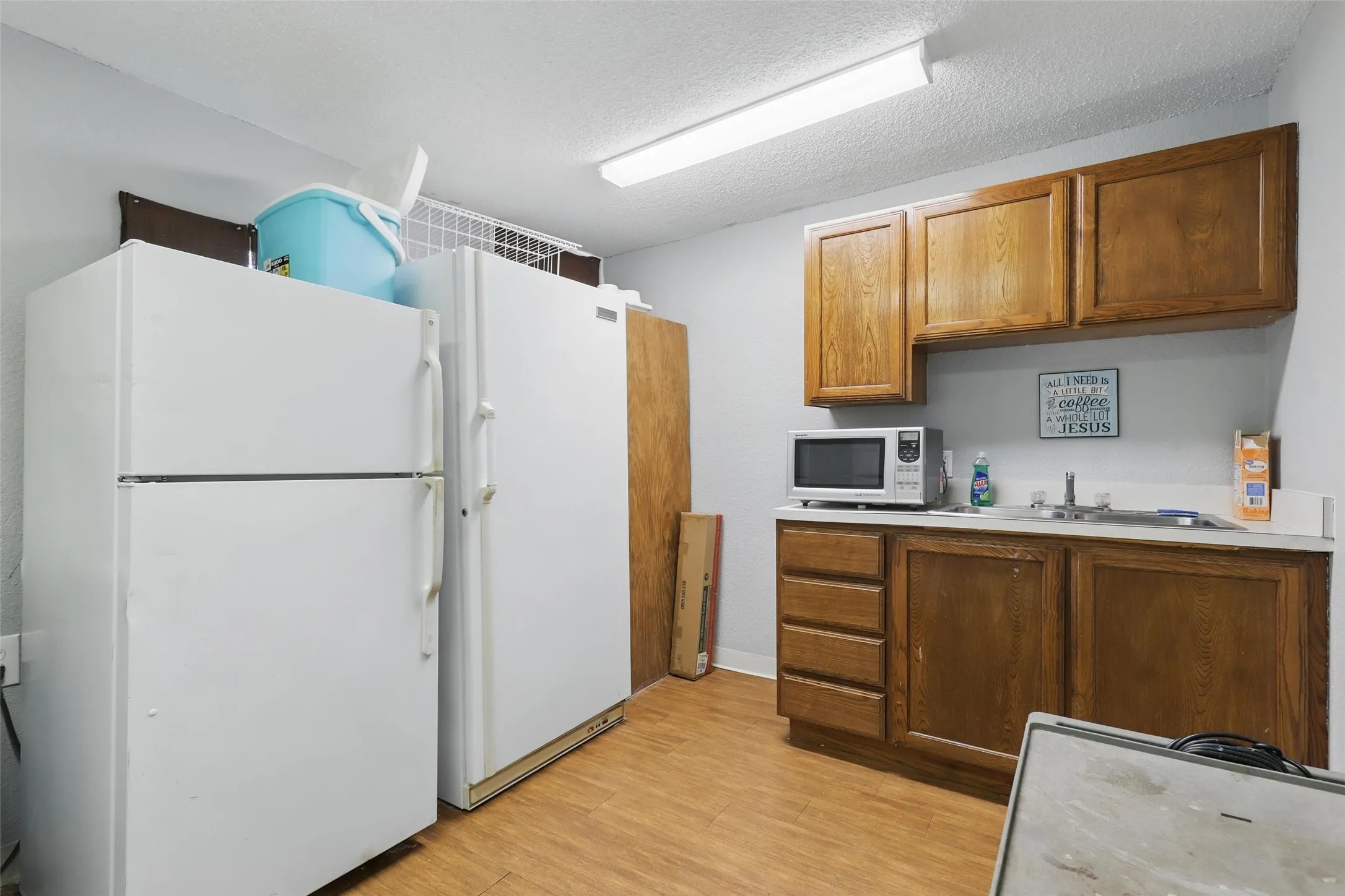 Kitchen with white appliances, a sink, brown cabinetry, light countertops, and light wood-style flooring