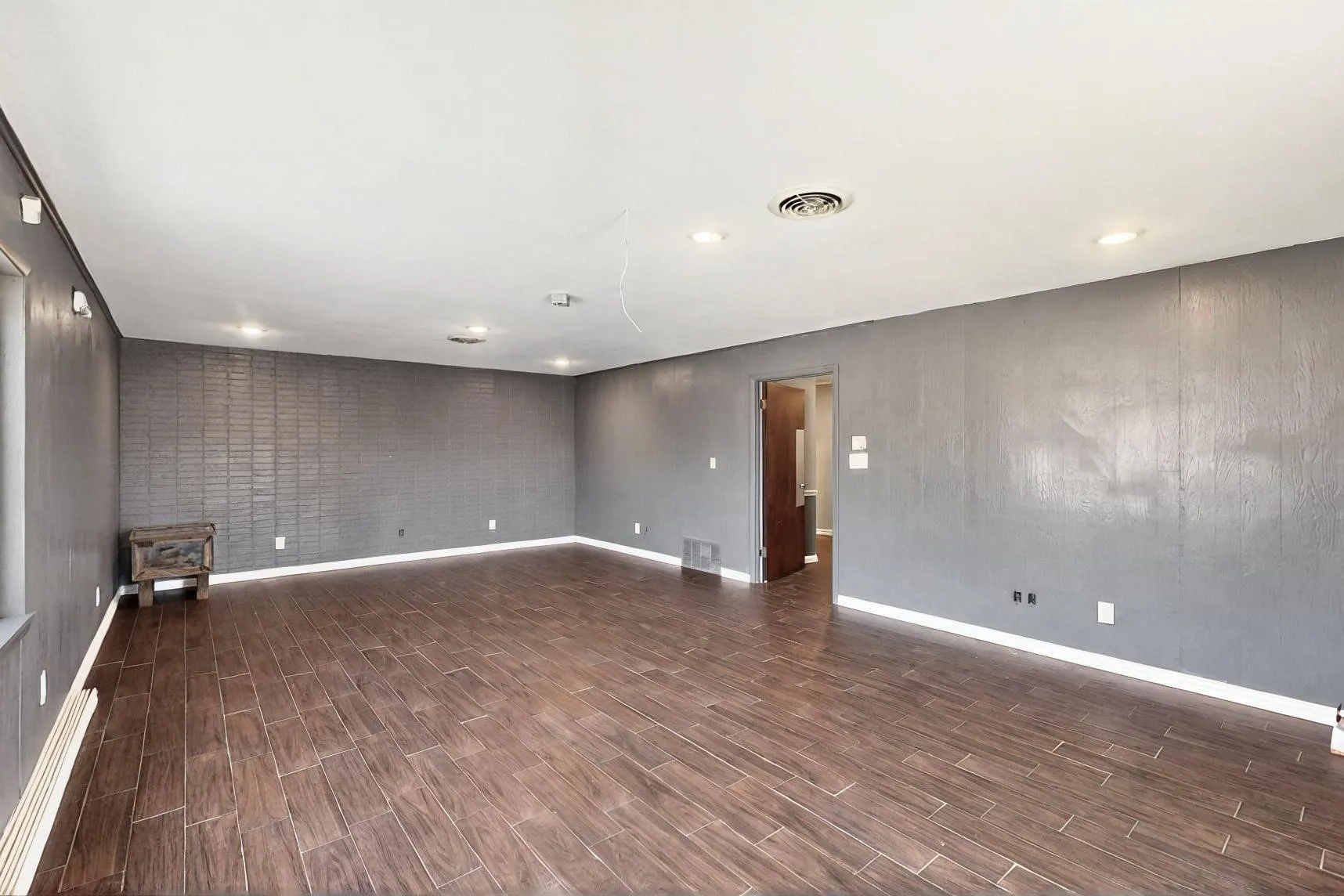 Empty room with wood tiled floors, baseboards, a wood stove, and brick wall