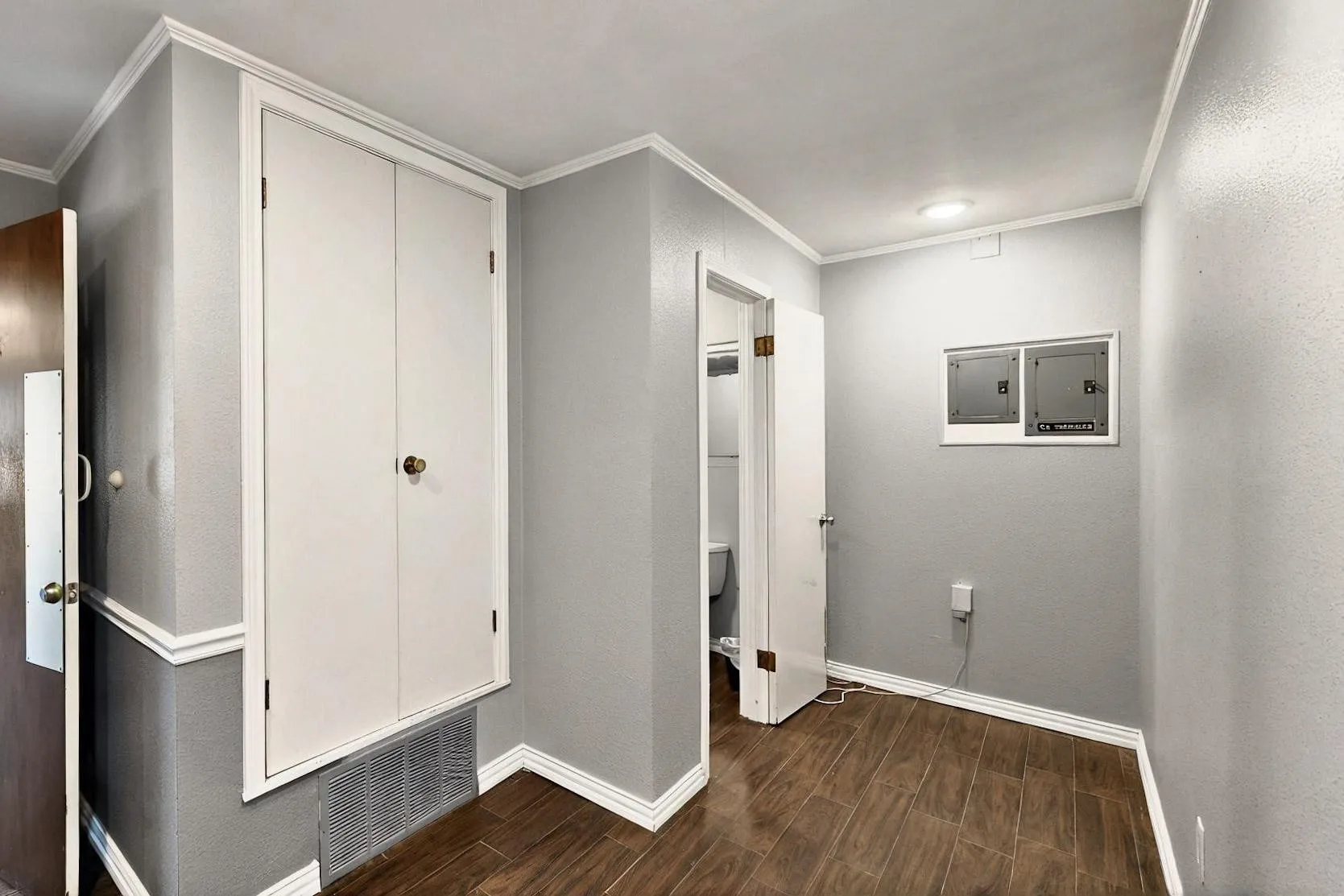 Corridor featuring dark wood-style flooring, baseboards, crown molding, and electric panel
